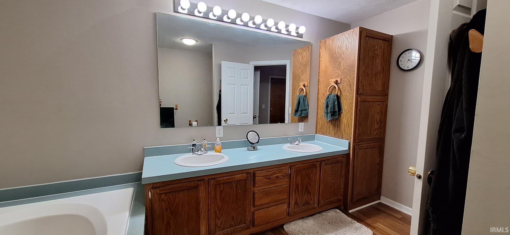 Full bath with double vanity, a bath, and light wood-type flooring