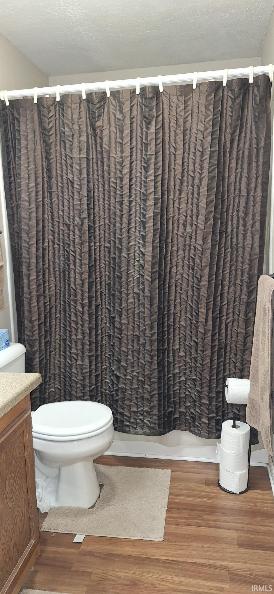 Bathroom with a textured ceiling, light wood-style flooring, curtained shower, and vanity