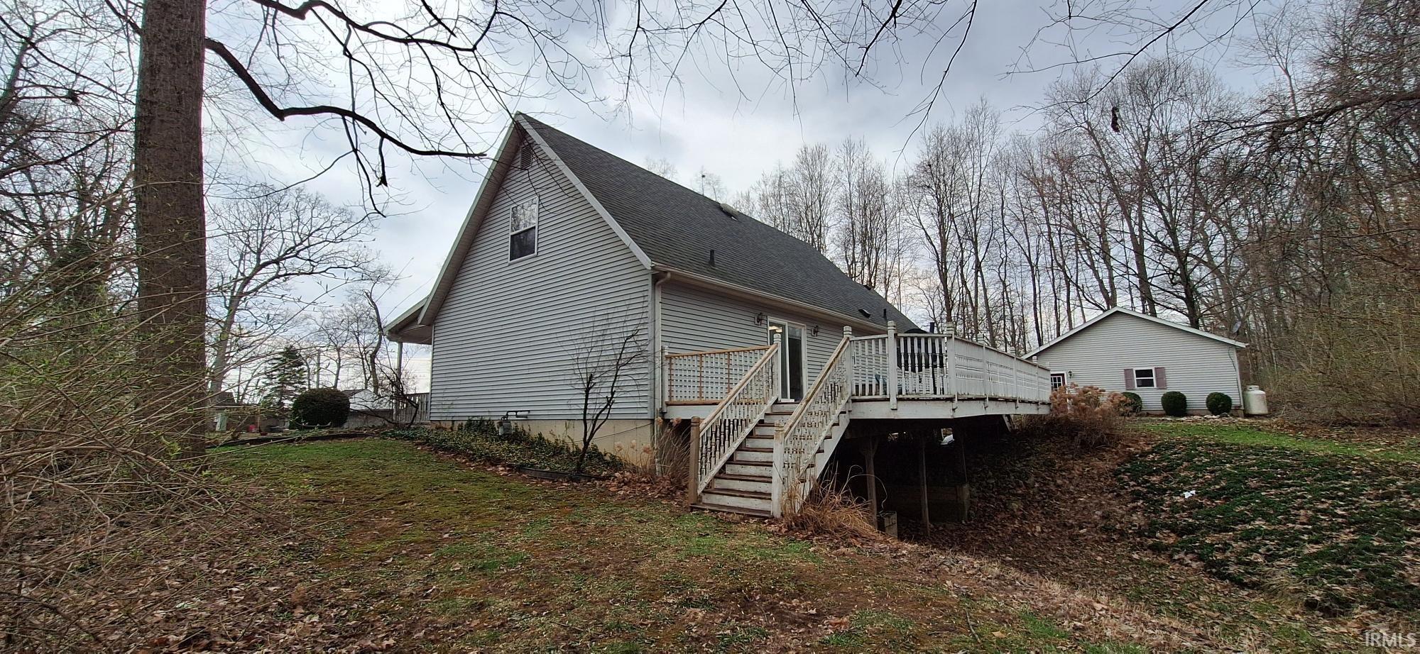 Back of property featuring a shingled roof, a deck, and a lawn