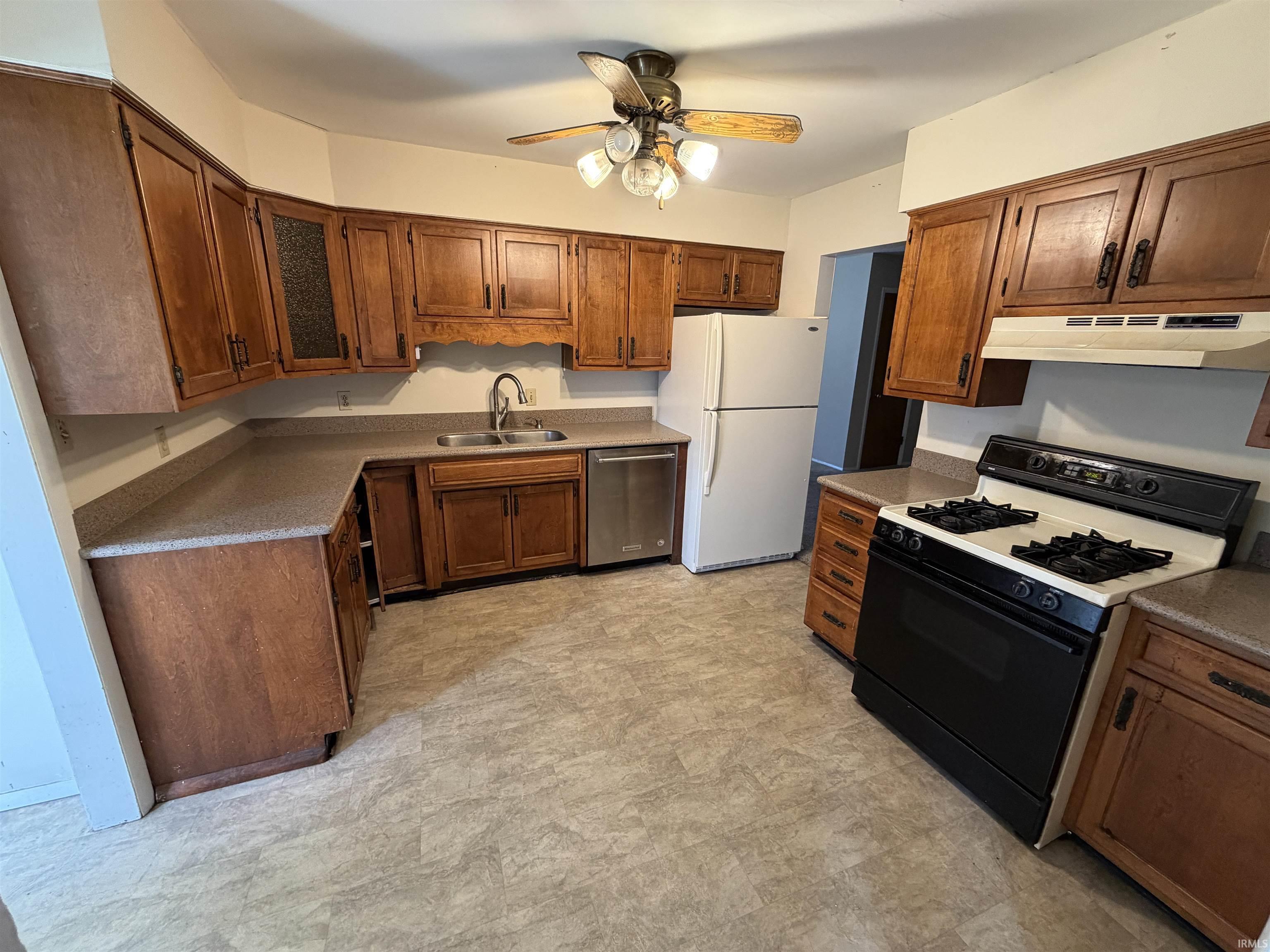 Kitchen featuring gas stove, ceiling fan, stainless steel dishwasher, freestanding refrigerator, and wood finish cabinetry