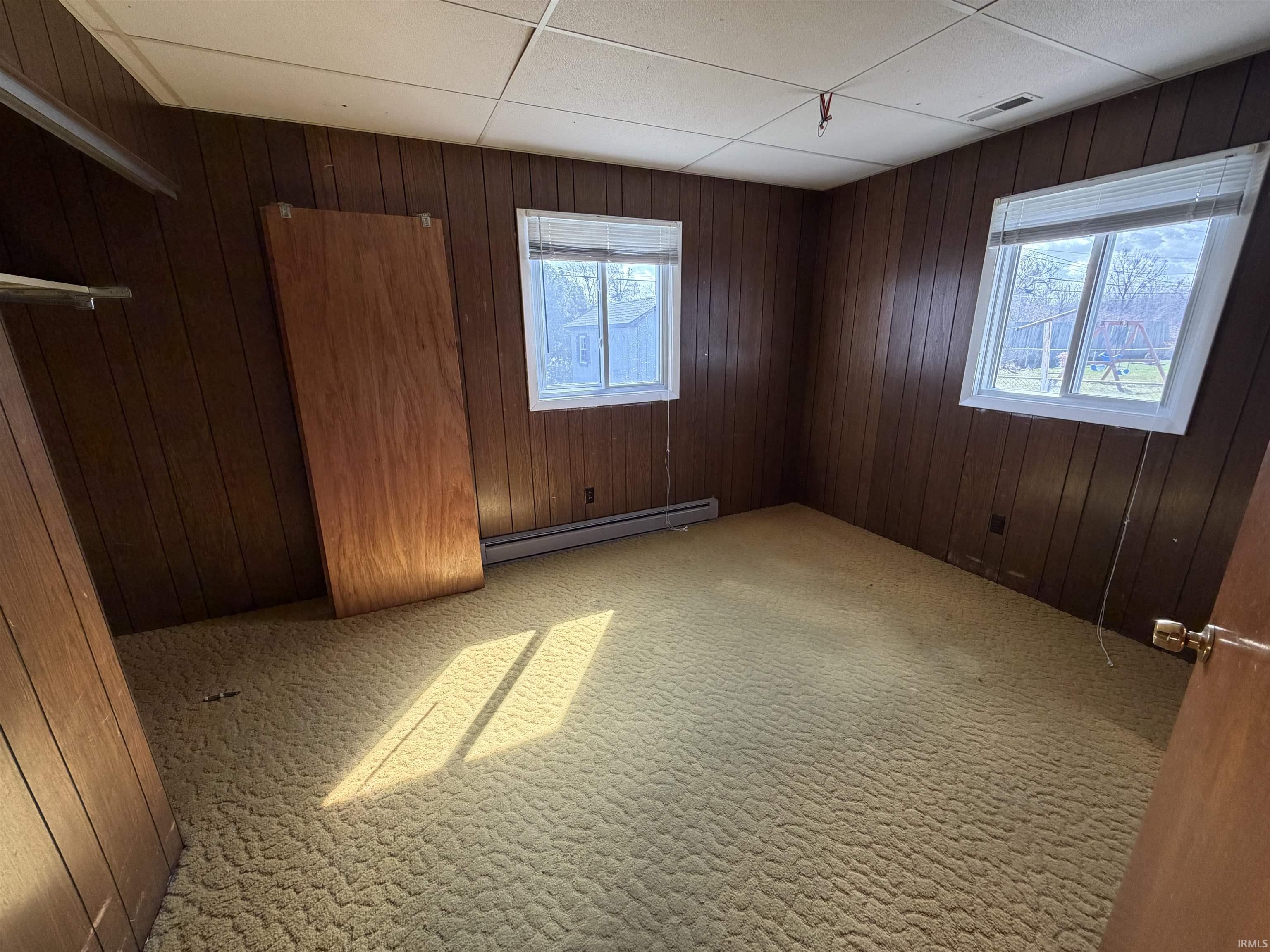 Unfurnished bedroom with wooden walls, light carpet, and a baseboard radiator