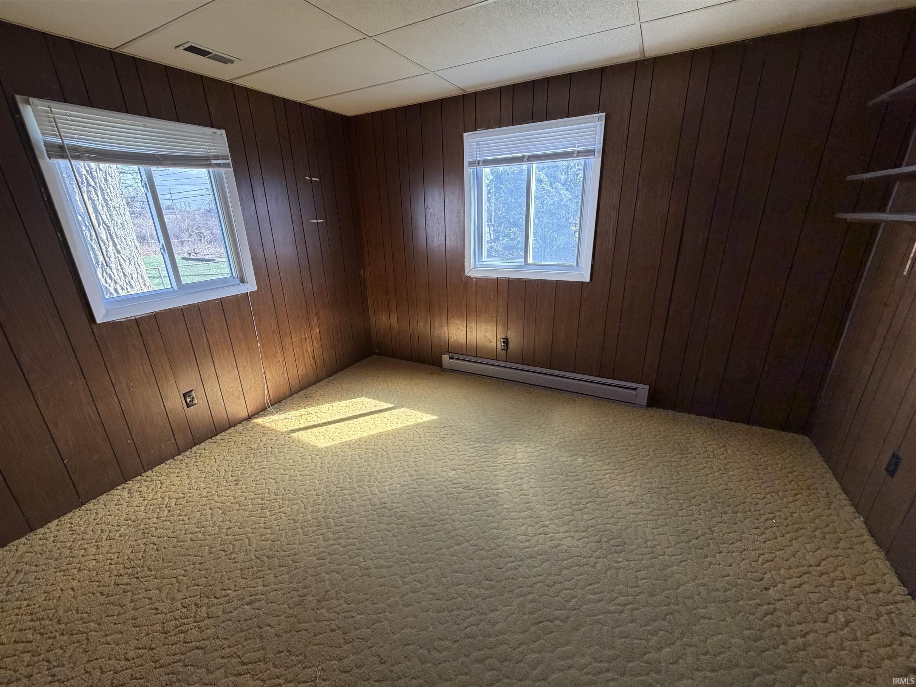 Spare room featuring wooden walls, light colored carpet, and a baseboard radiator