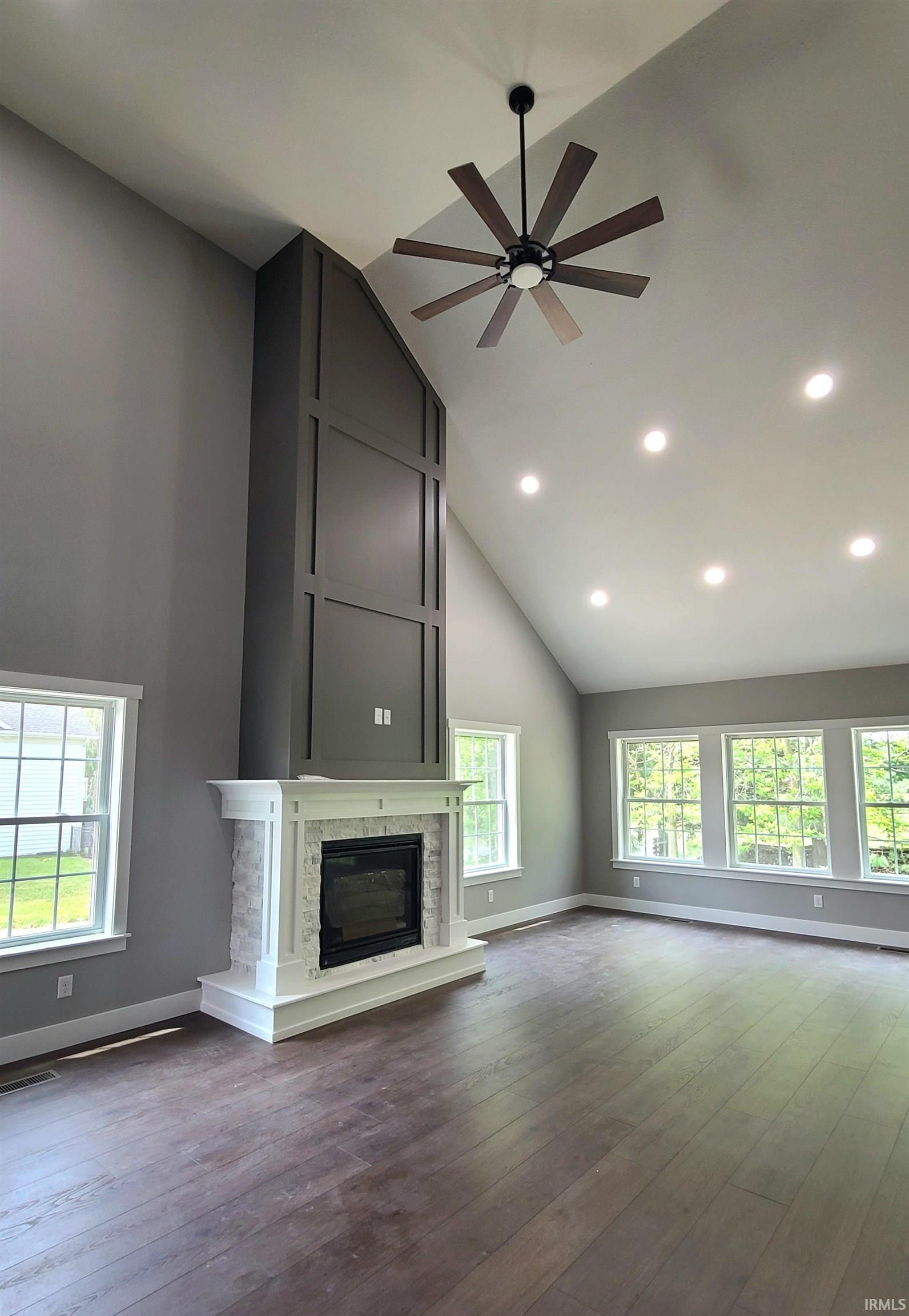 Unfurnished living room with a glass covered fireplace, dark wood-style floors, vaulted ceiling, ceiling fan, and plenty of natural light