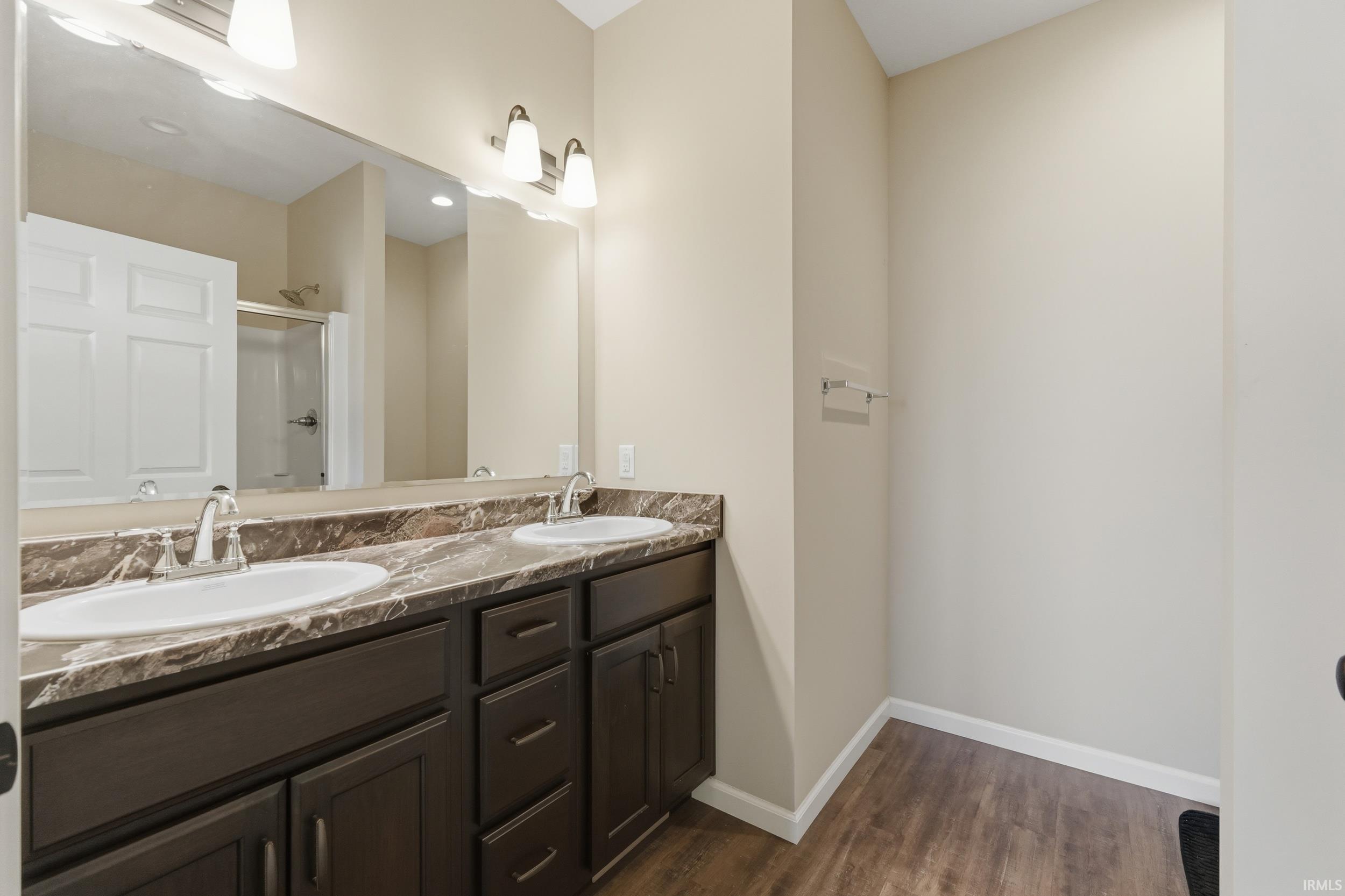 Bathroom featuring double vanity, a stall shower, and dark wood-type flooring