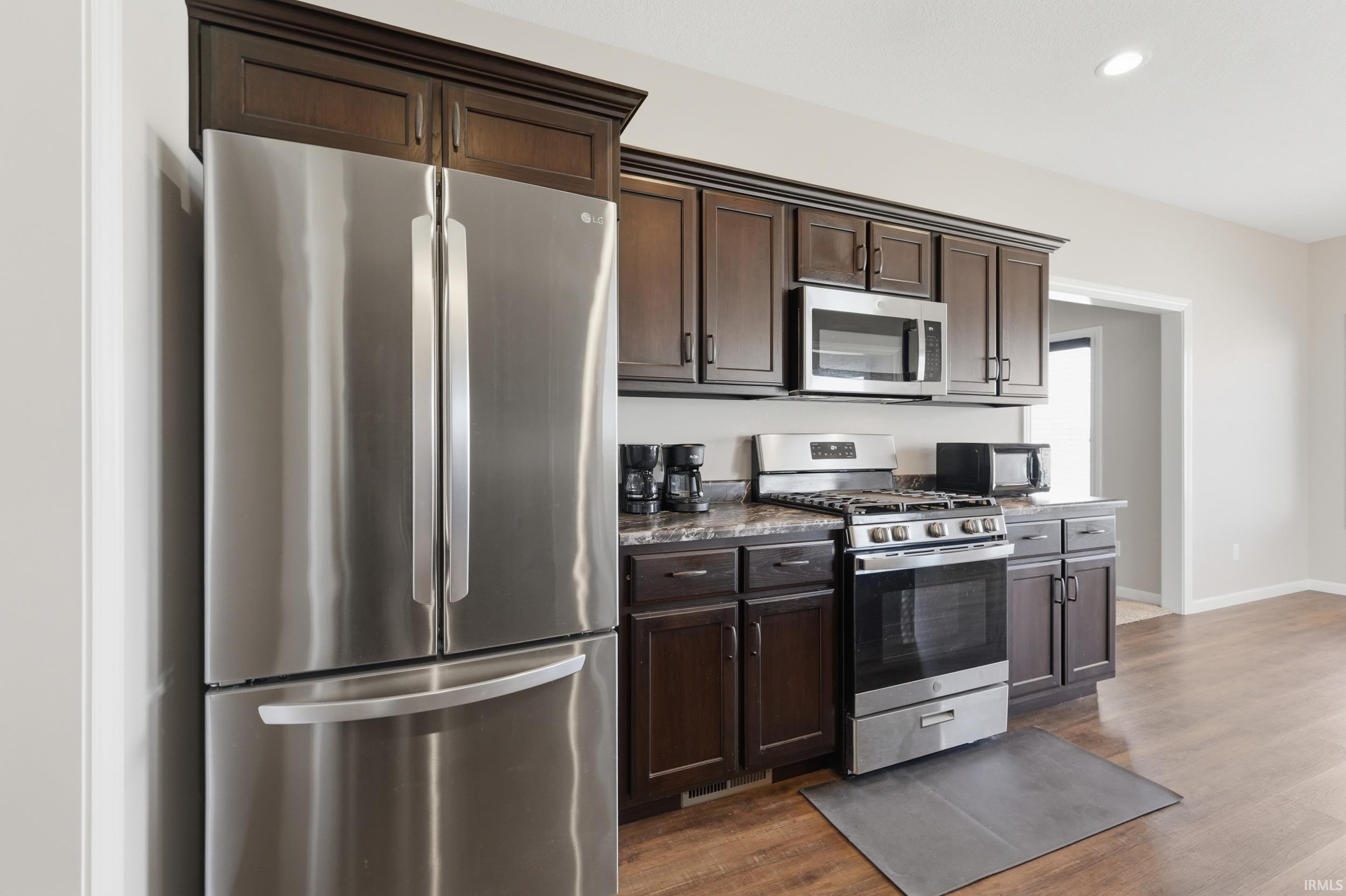 Kitchen with stainless steel appliances, dark wood finish cabinets, recessed lighting, dark wood-style floors, and dark stone counters