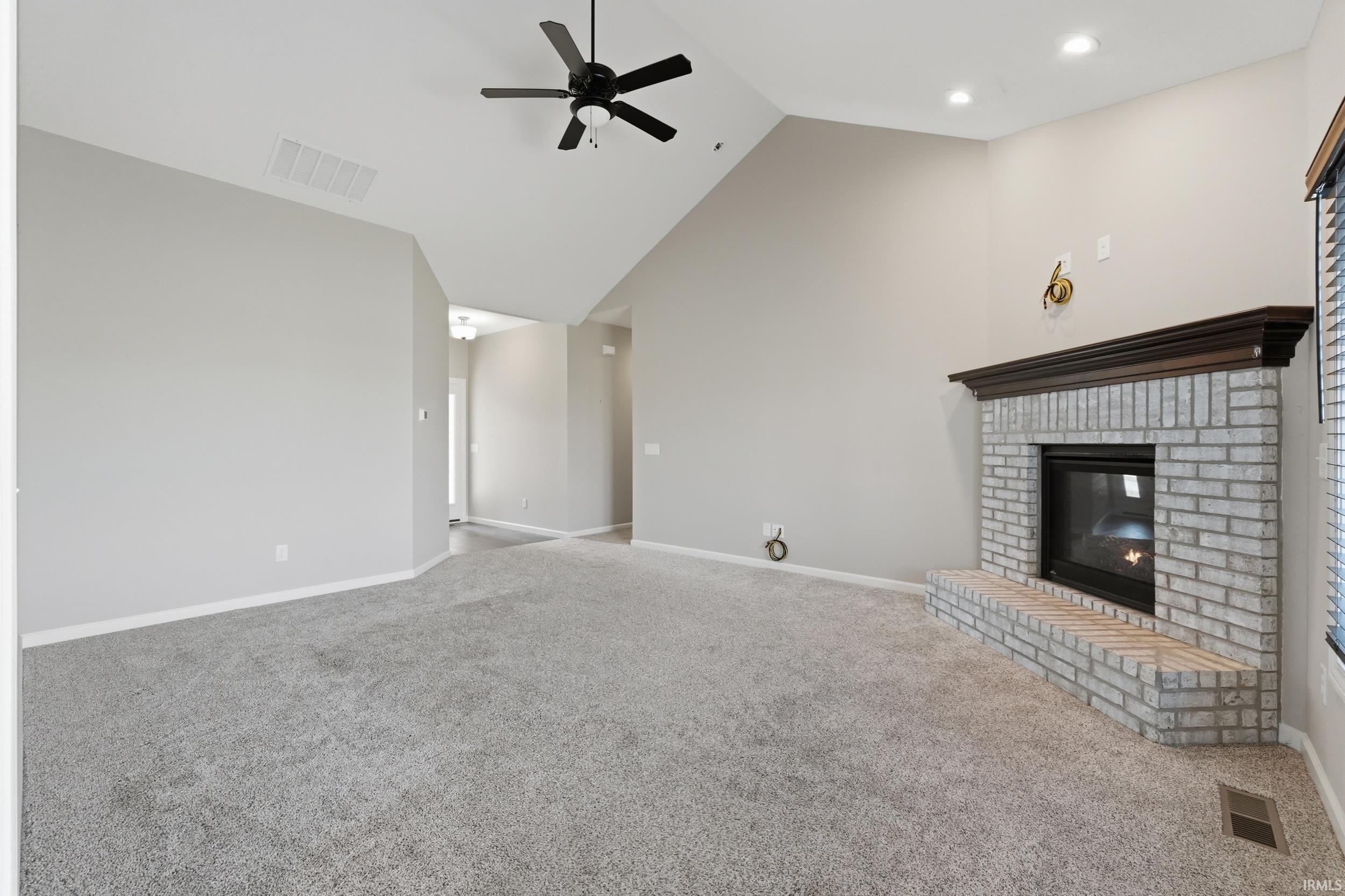 Unfurnished living room featuring a fireplace, lofted ceiling, carpet floors, and ceiling fan