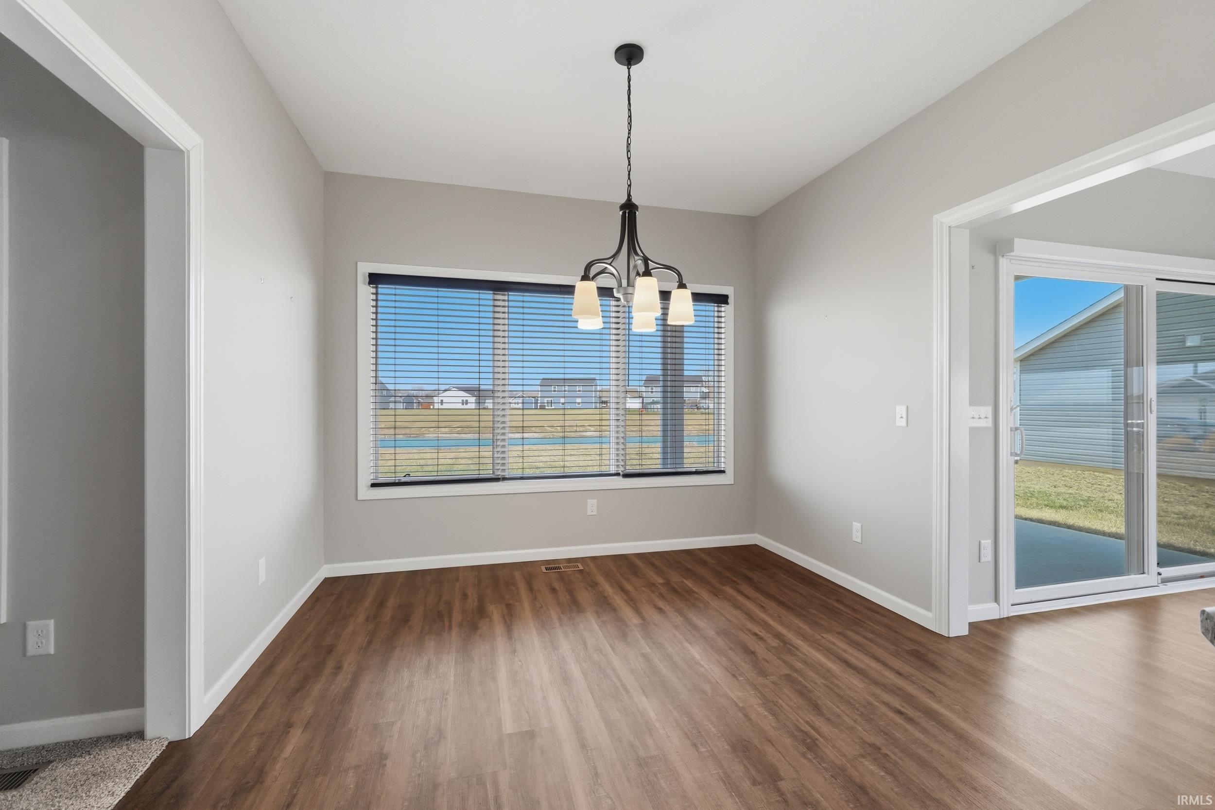 Unfurnished dining area with hanging lights, dark wood finished floors, and plenty of natural light