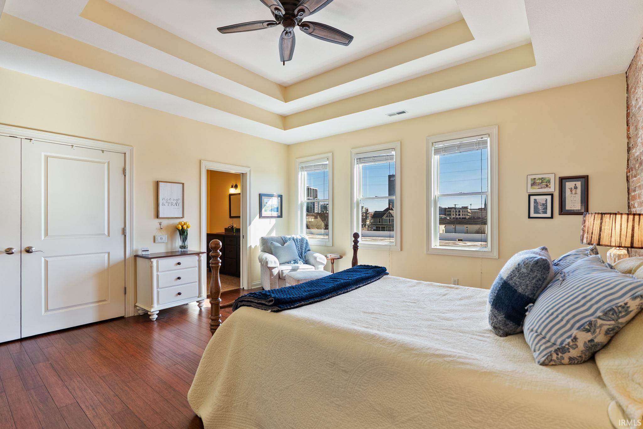 Bedroom with ensuite bathroom, dark wood-style flooring, ceiling fan, and a tray ceiling