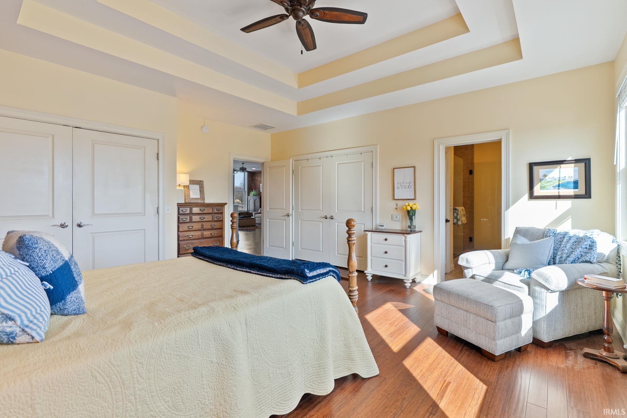 Bedroom featuring multiple closets, a raised ceiling, dark wood finished floors, and ceiling fan
