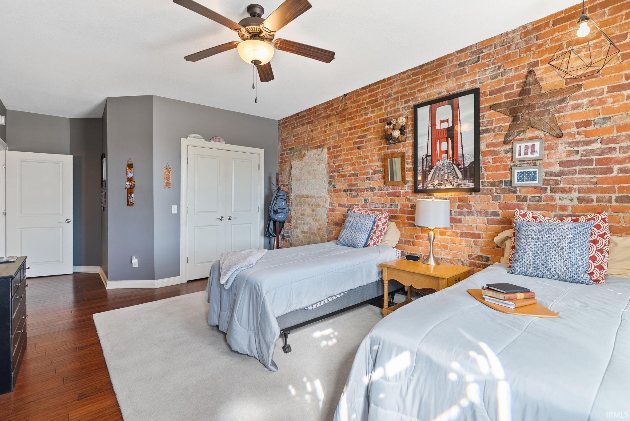 Bedroom featuring brick wall, dark wood-style flooring, ceiling fan, and a closet