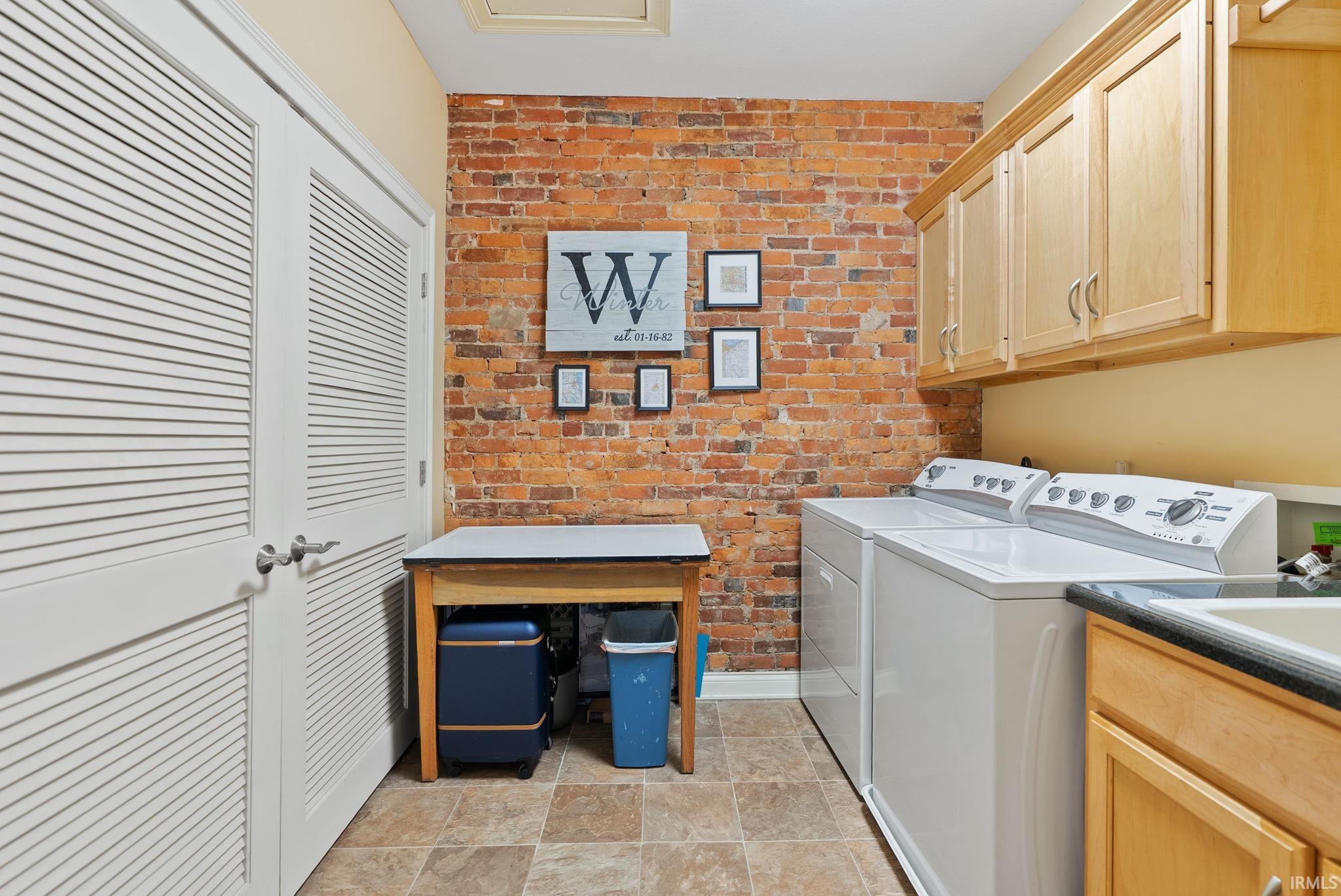 Laundry room with brick wall, independent washer and dryer, stone finish floors, and cabinet space