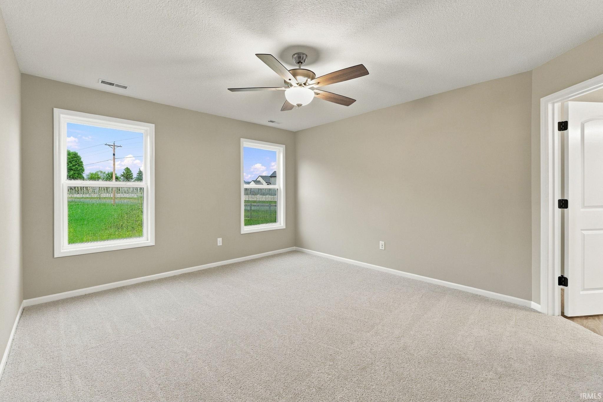 Neutral wall tones, light carpet flooring, two large windows, and a ceiling fan with integrated lighting