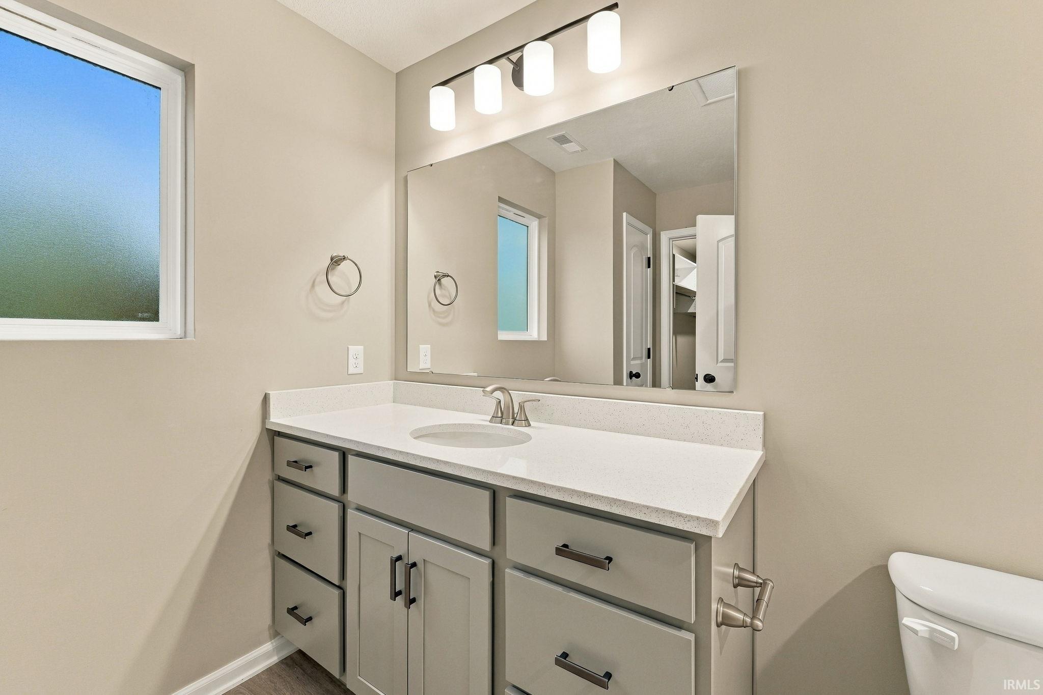 White vanity with a built-in sink, stainless steel faucet, and overhead bar lighting