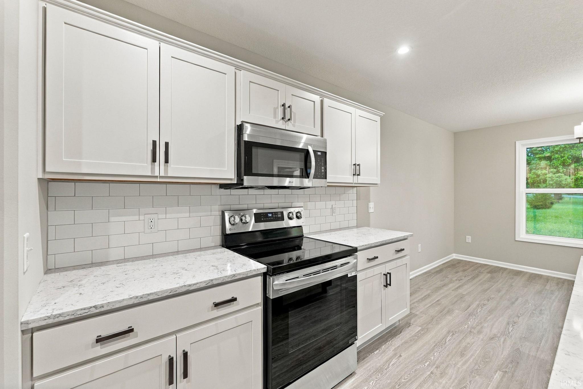 White shaker cabinetry, stainless steel appliances, white subway tile backsplash, light-toned wood-finish flooring, and light-toned countertops