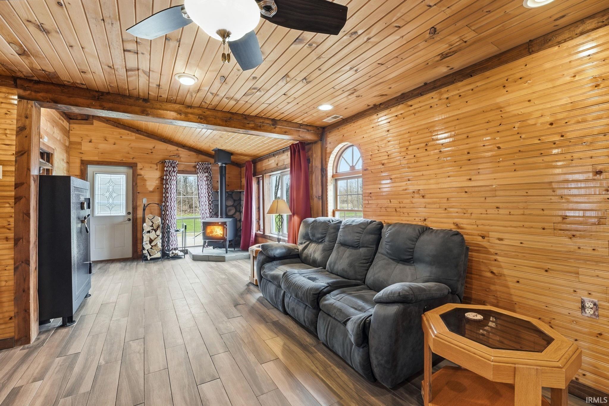 Living room with wood walls, wood finish floors, a wood stove, a ceiling fan, and recessed lighting
