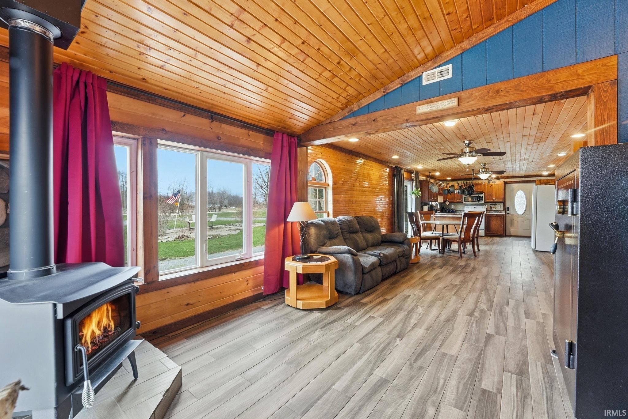Living area featuring a wood stove, a vaulted wooden ceiling, light wood-type flooring, wooden walls, and ceiling fan