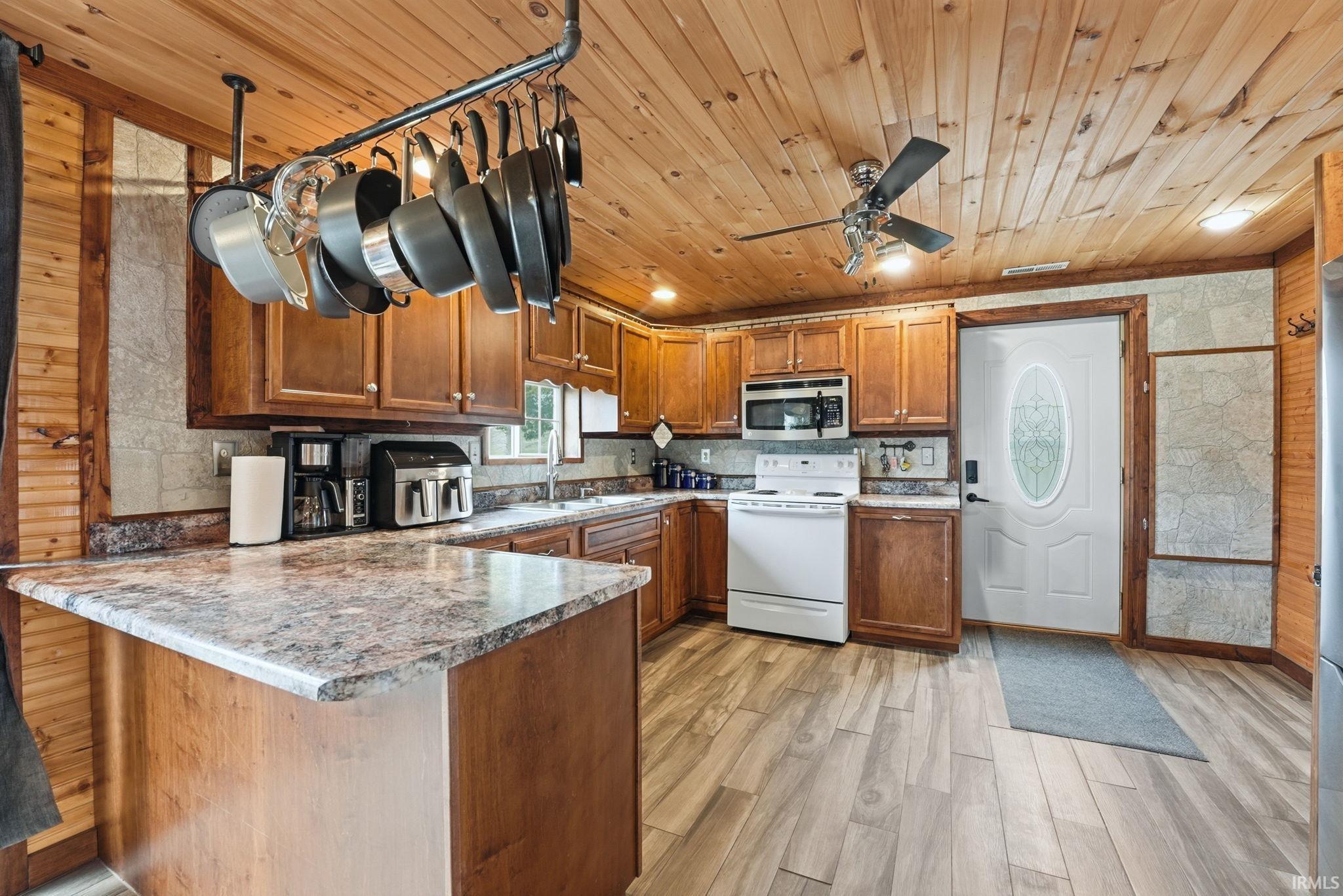 Kitchen featuring wood finish cabinetry, a peninsula, white electric range oven, light wood-style floors, and stainless steel microwave