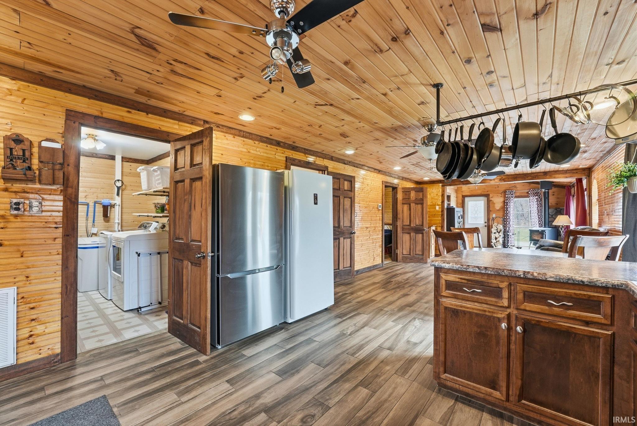 Kitchen with ceiling fan, wood walls, dark countertops, freestanding refrigerator, and dark wood finished floors