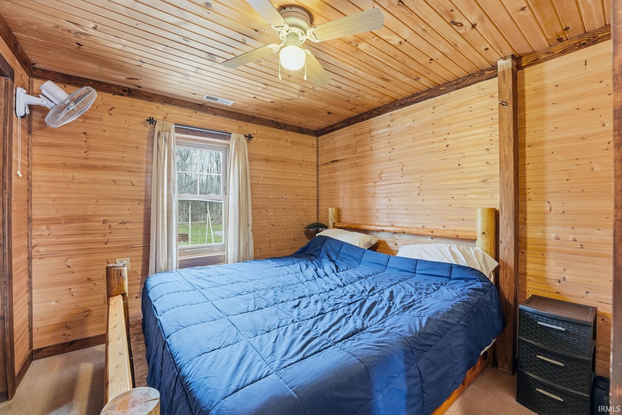 Bedroom with wood walls, ceiling fan, wood ceiling, and carpet
