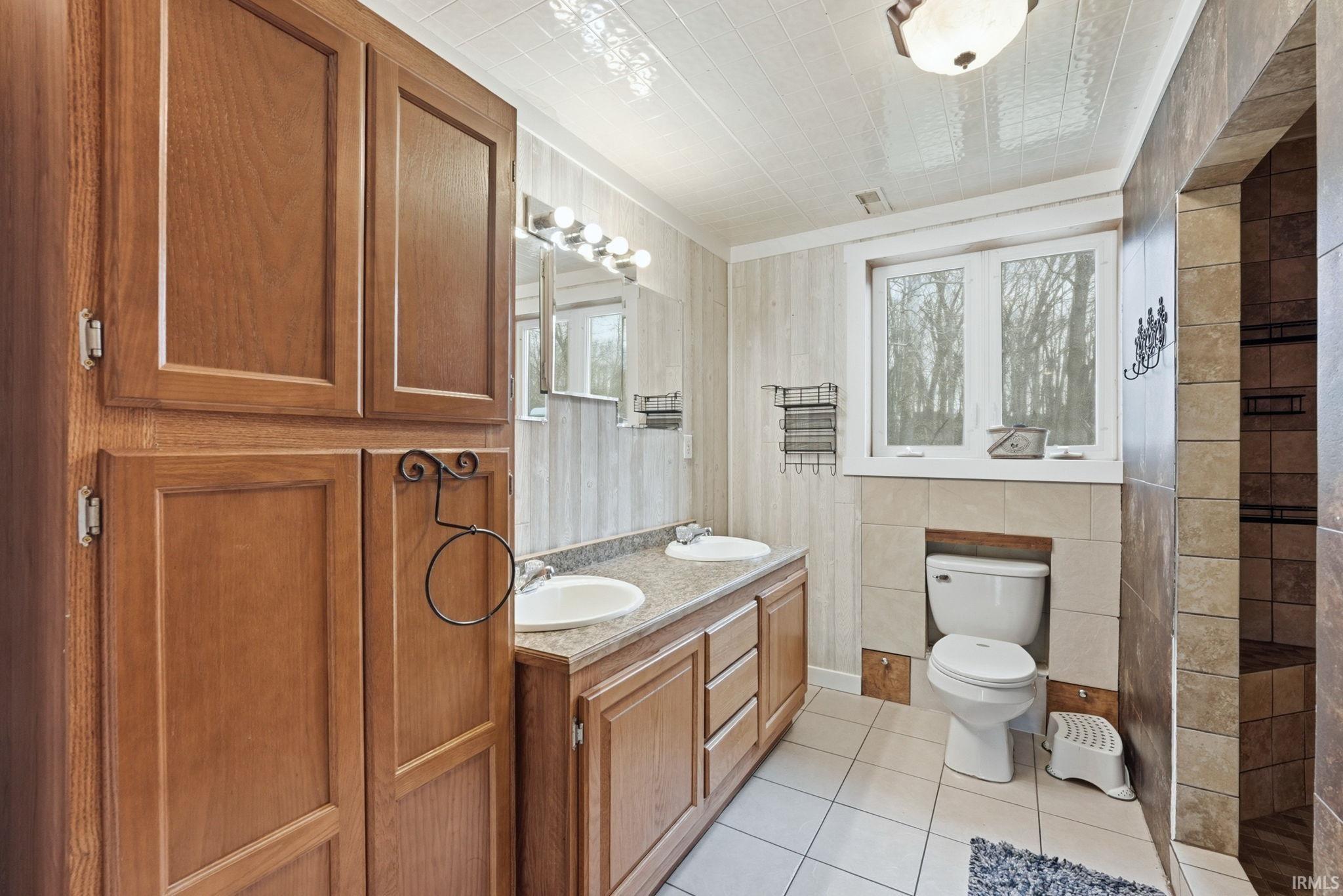 Bathroom with double vanity, light tile patterned floors, and a walk in shower