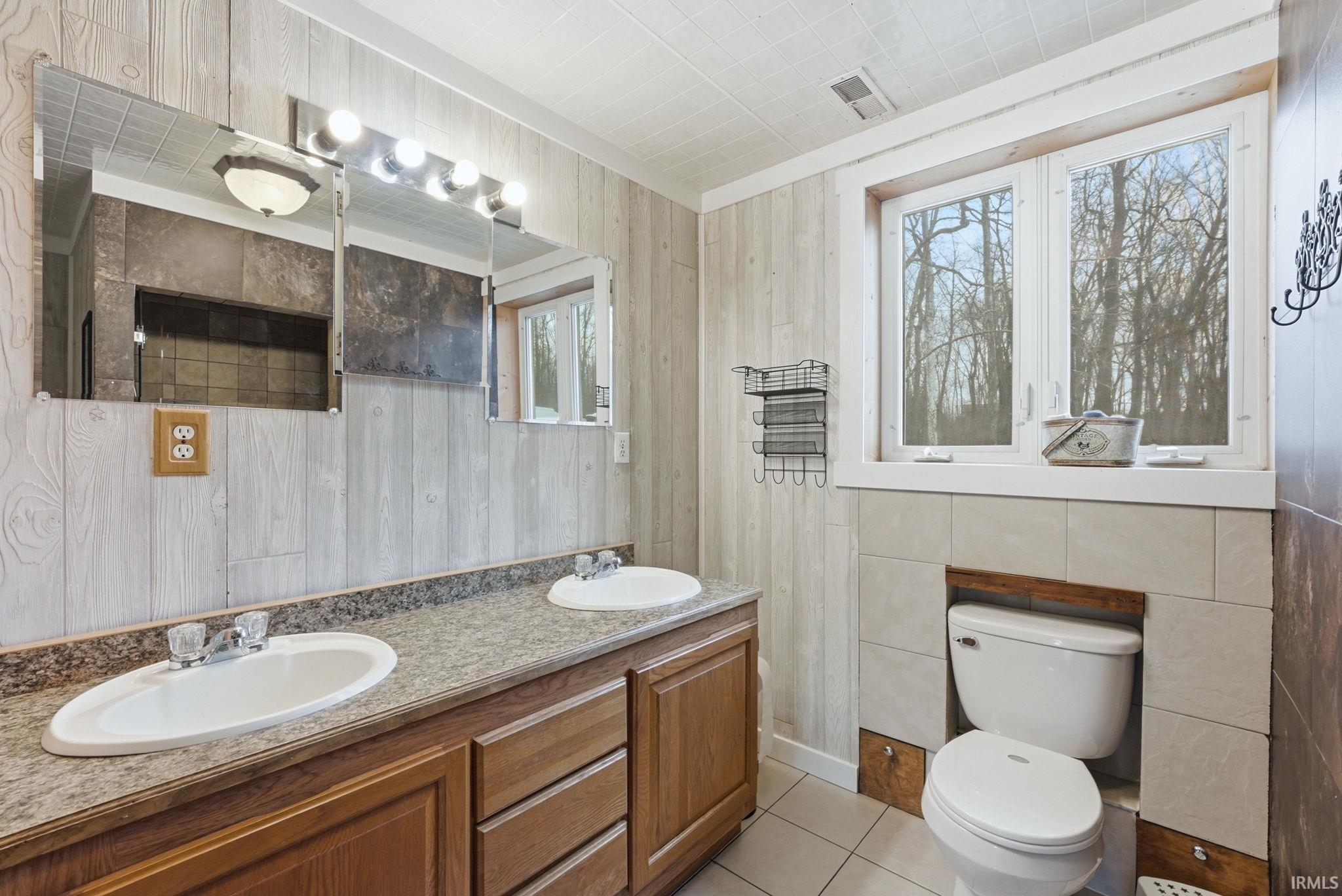 Full bathroom featuring double vanity, light tile patterned floors, and wood walls
