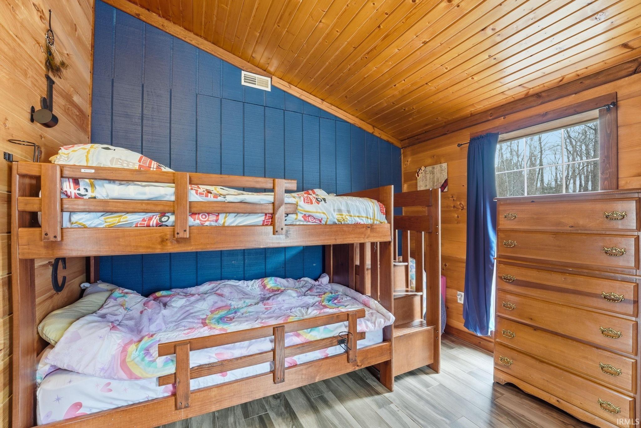Bedroom with wood walls, a vaulted wooden ceiling, and wood finished floors