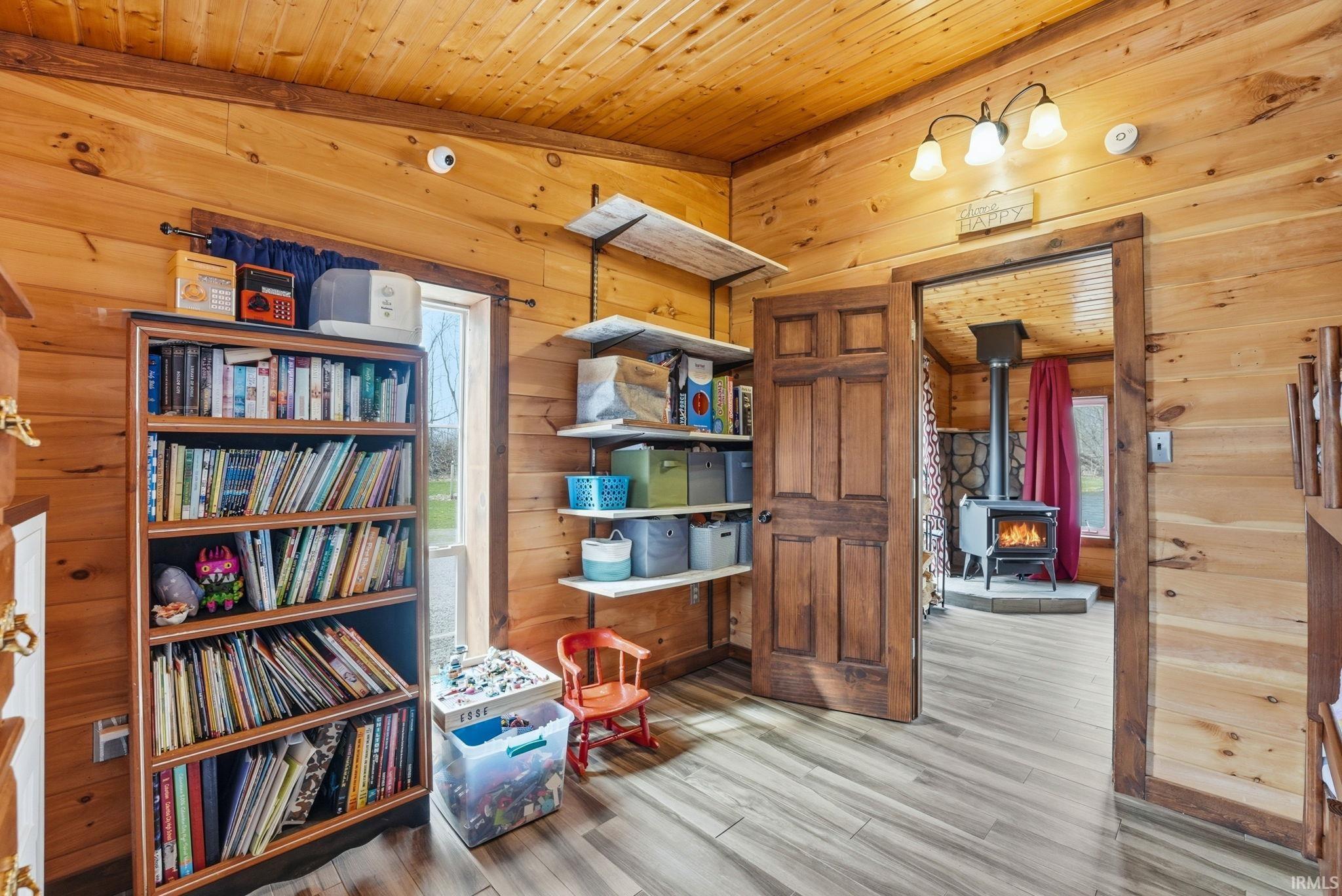 Sitting room with wood ceiling, light wood finished floors, wooden walls, and a wood stove