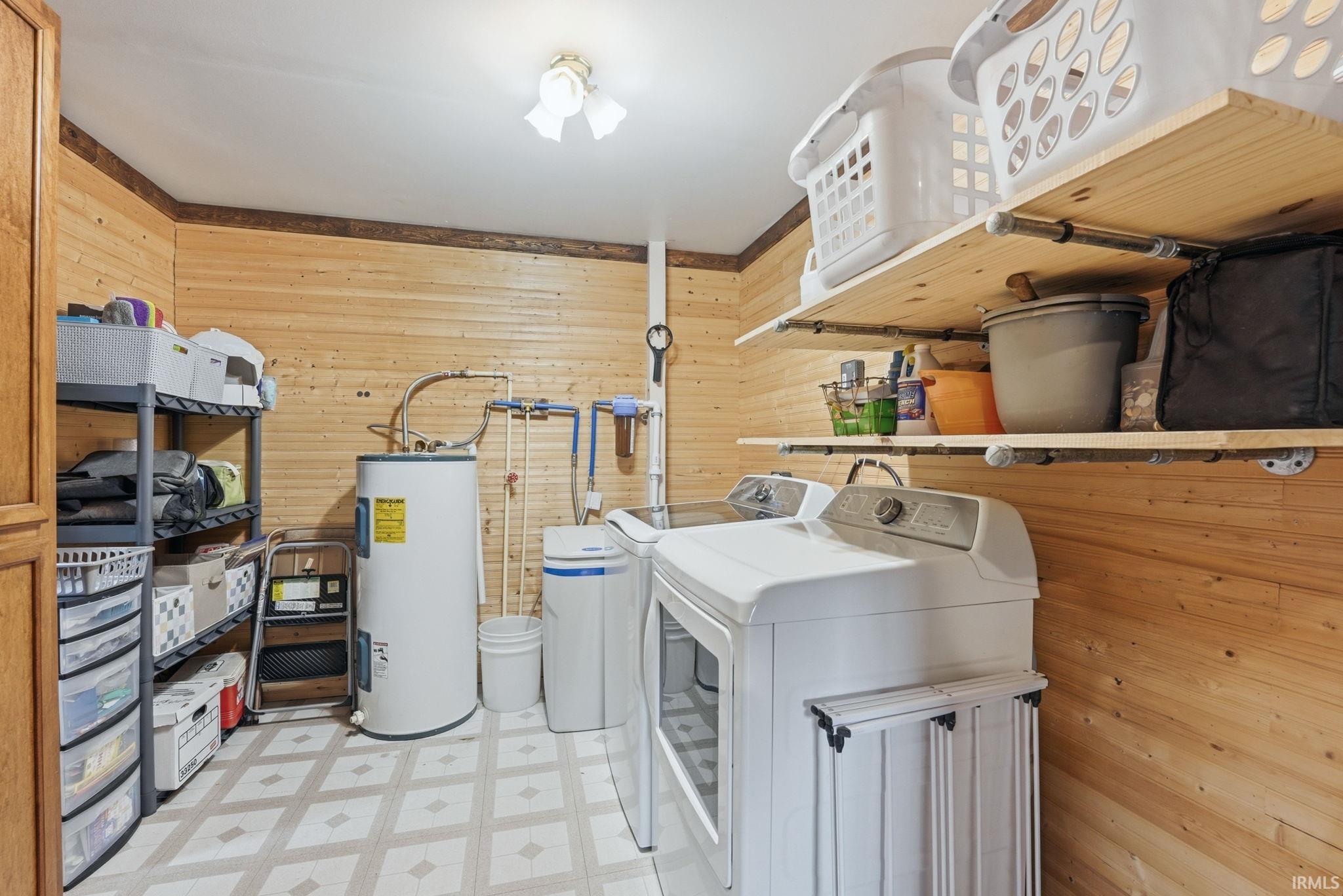 Laundry area with light flooring, wood walls, water heater, and washing machine and clothes dryer