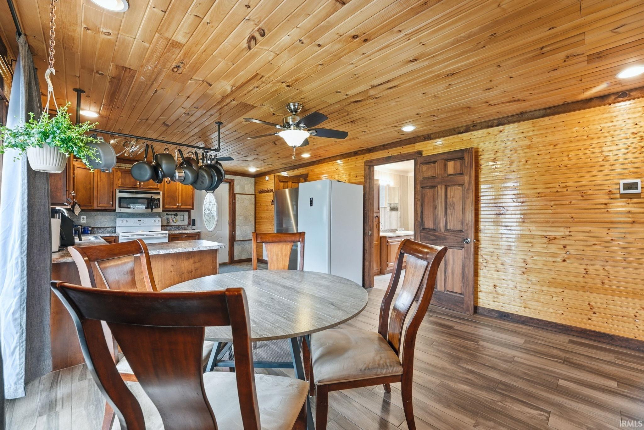 Dining room with light wood finished floors, wood walls, ceiling fan, and wood ceiling