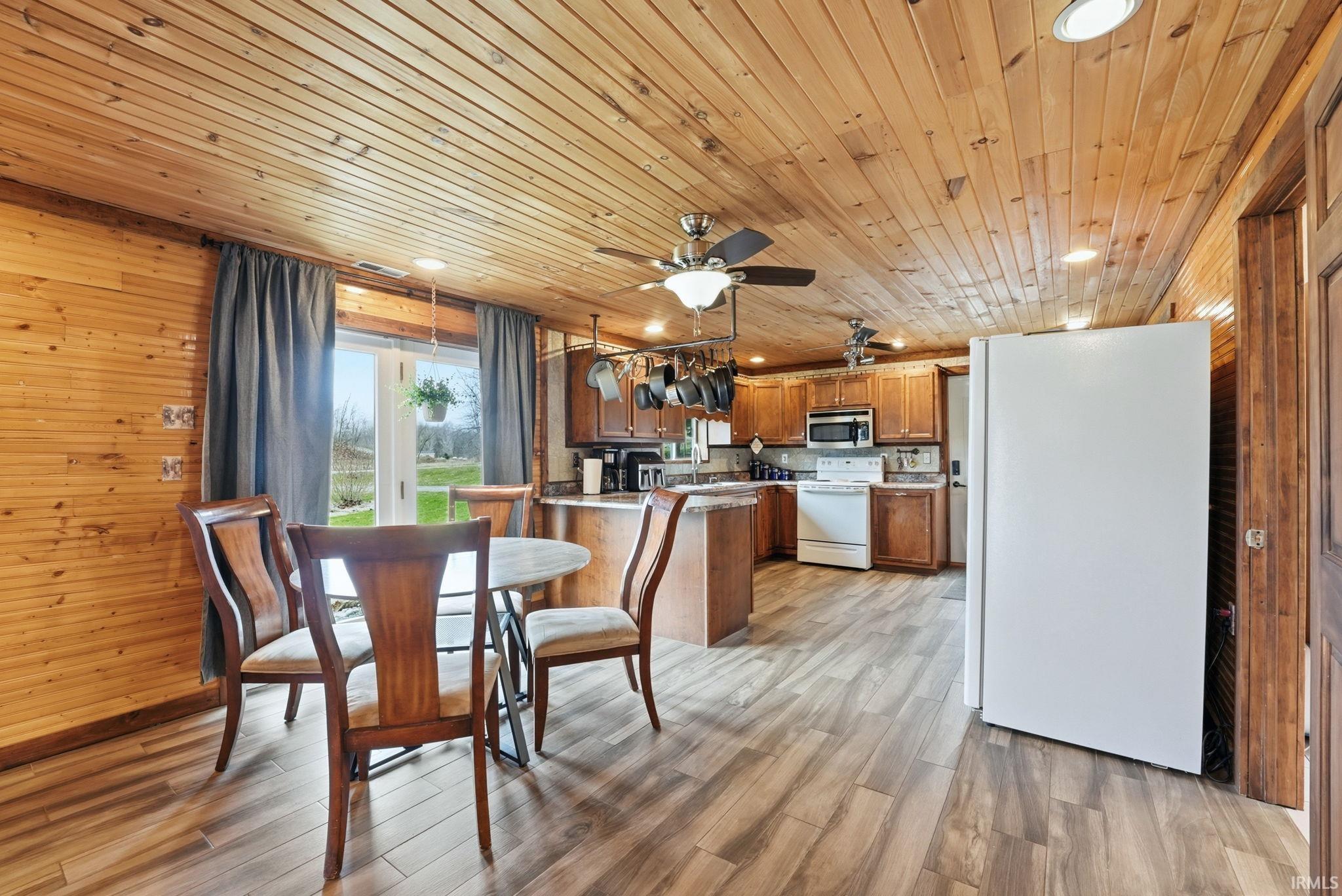 Dining area featuring light wood finished floors, a ceiling fan, wood walls, and wood ceiling
