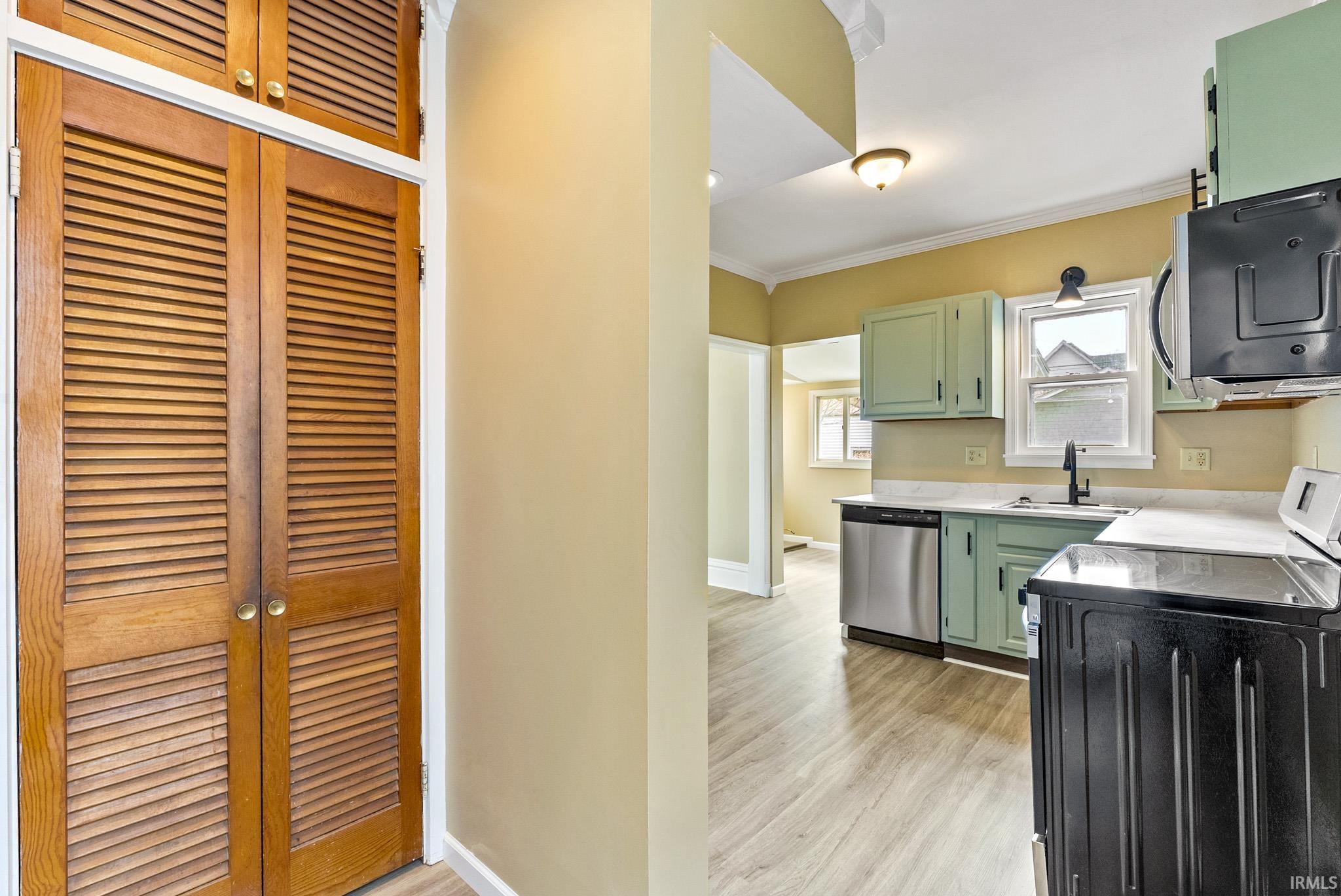 Kitchen featuring green cabinetry, ornamental molding, light countertops, stainless steel appliances, and light wood-style flooring