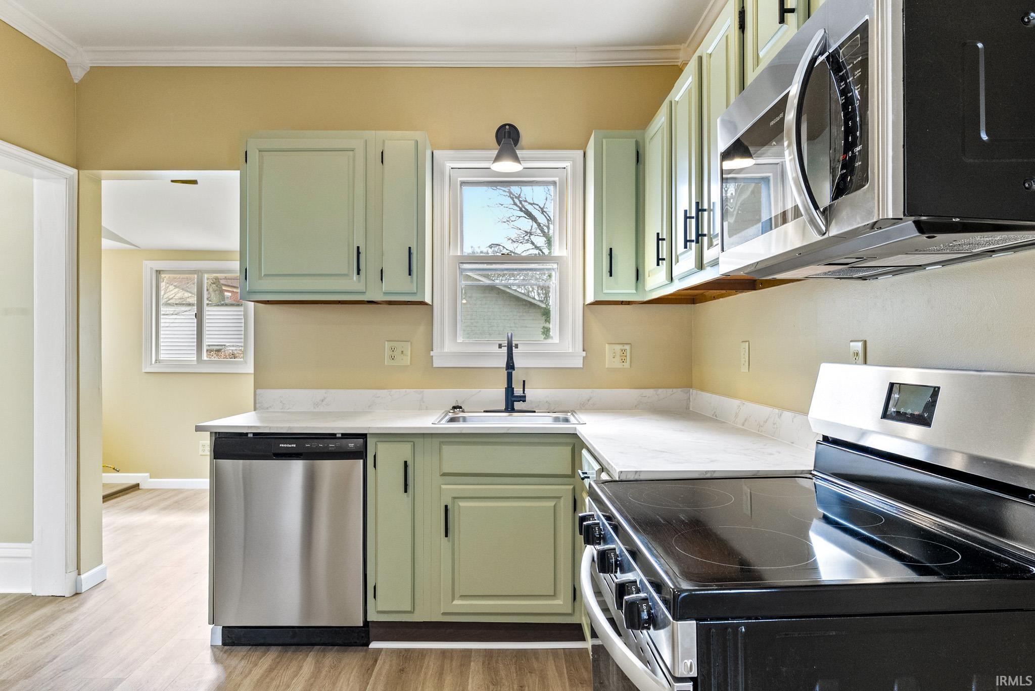 Kitchen with green cabinetry, stainless steel appliances, light countertops, light wood-style flooring, and crown molding