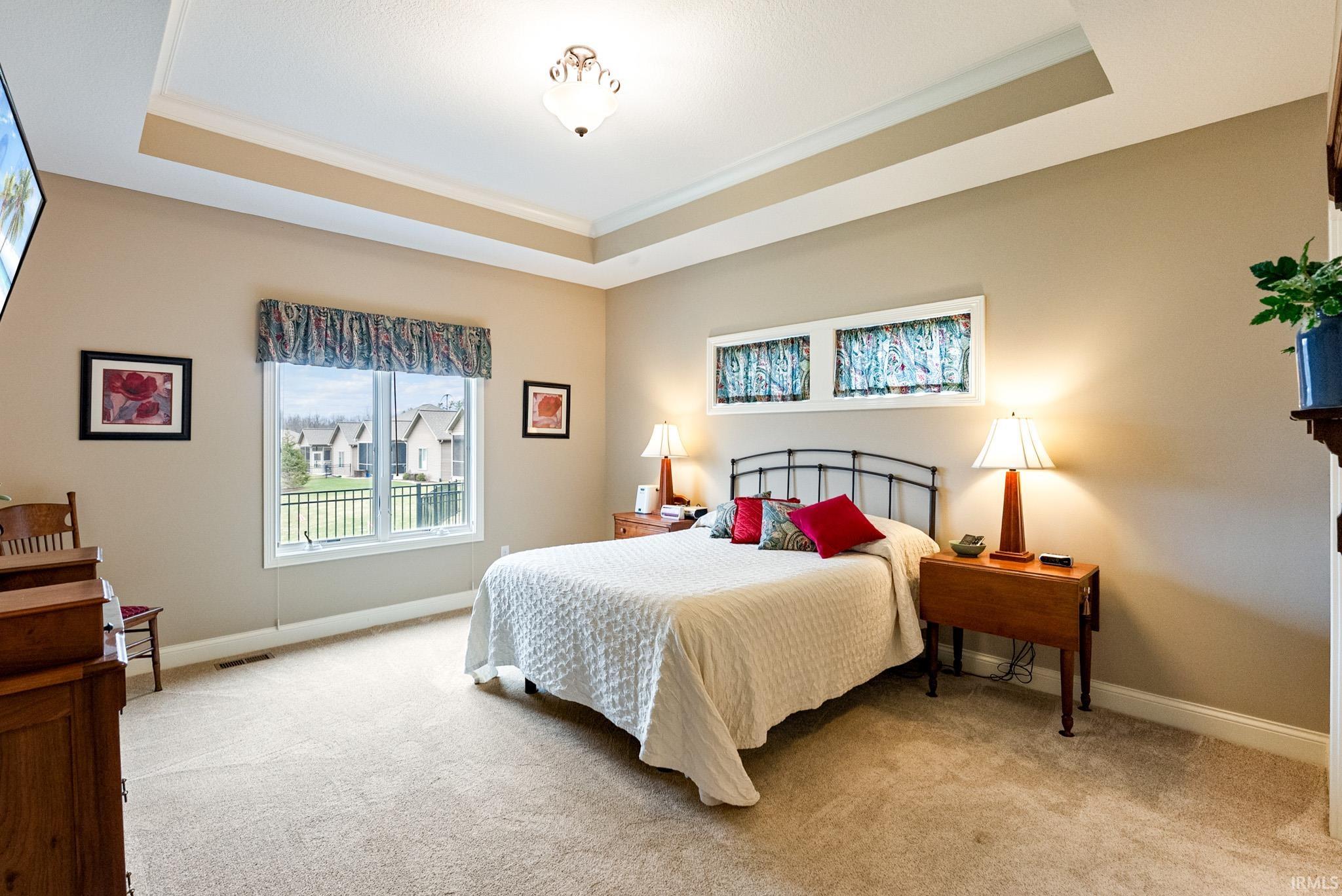 Bedroom featuring light carpet, a tray ceiling, and ornamental molding