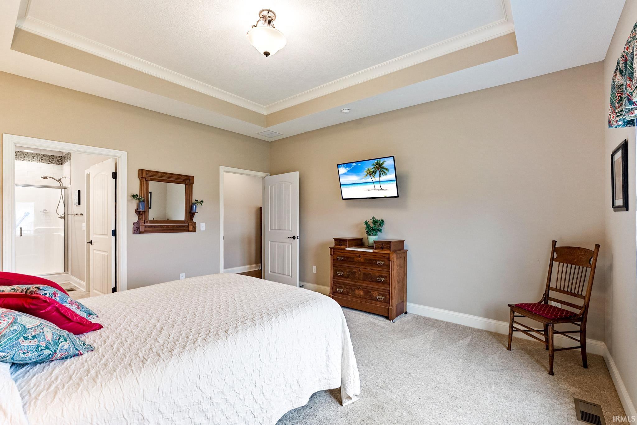Carpeted bedroom with ornamental molding, a tray ceiling, and ensuite bathroom