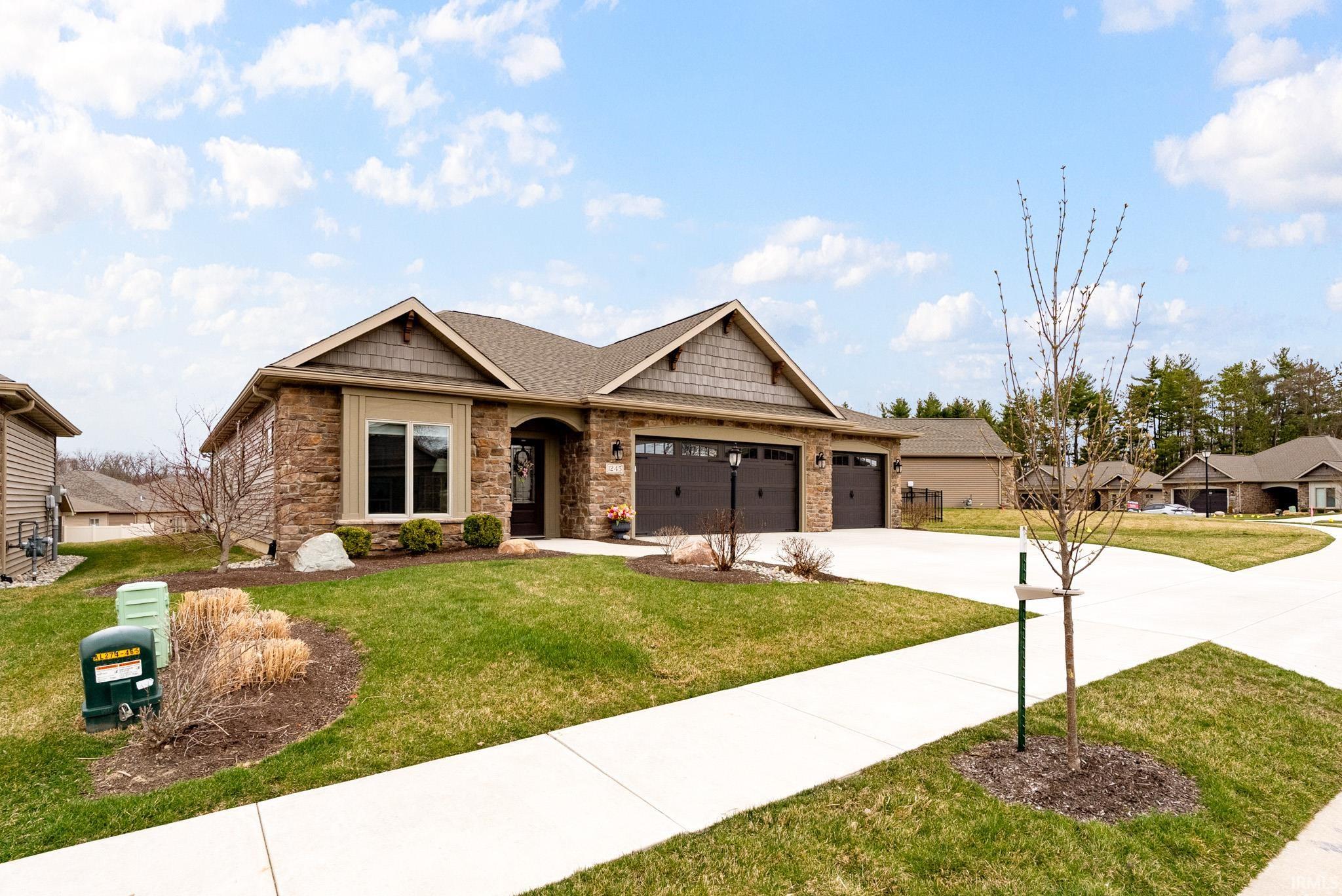 Craftsman house with stone siding, an attached garage, driveway, and a front yard