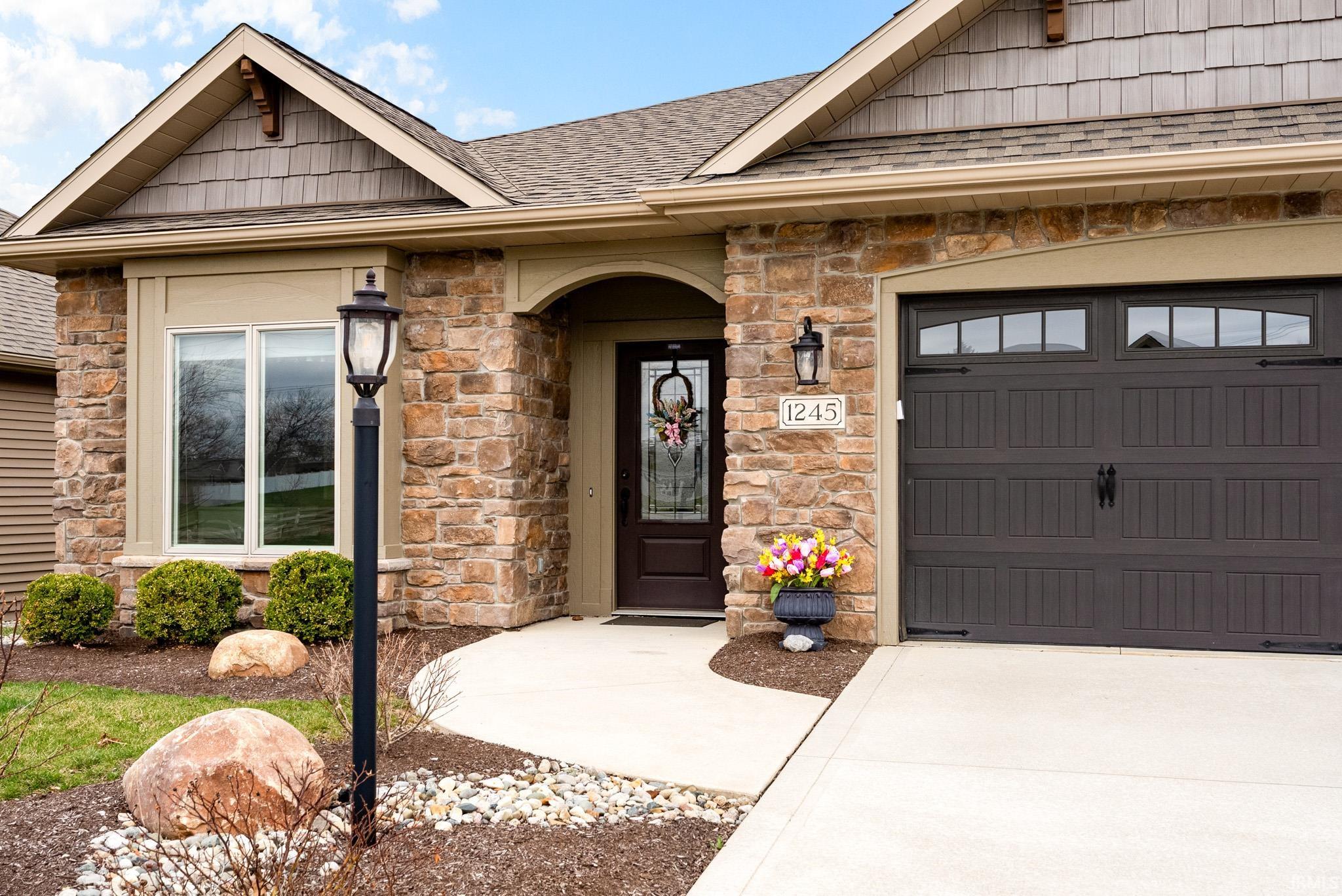View of exterior entry with stone siding, a shingled roof, and concrete driveway