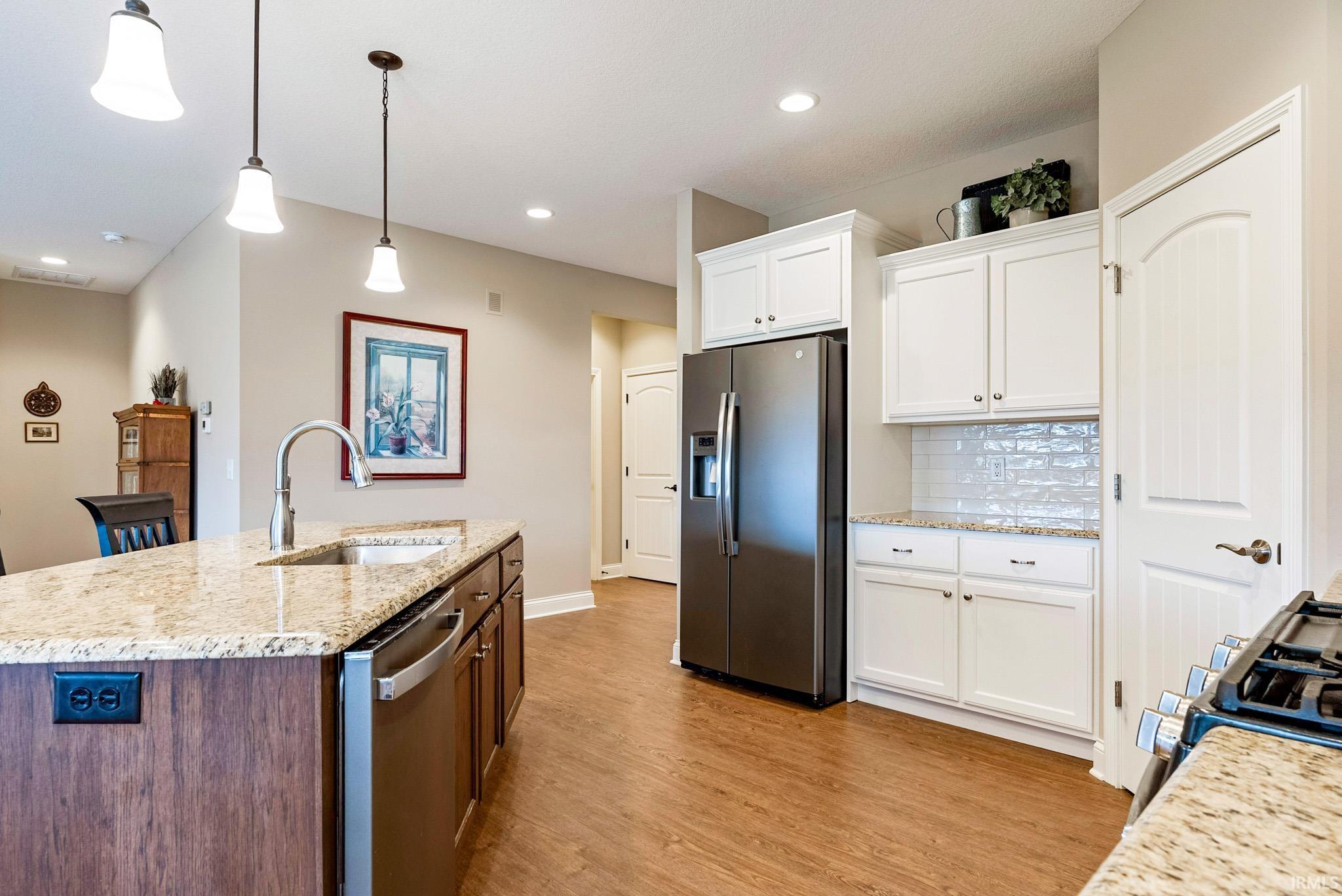 Kitchen with stainless steel appliances, light stone counters, hanging light fixtures, light wood-type flooring, and a kitchen island with sink