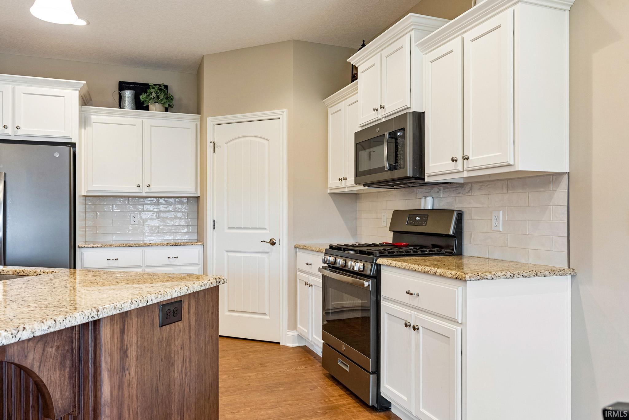 Two tone kitchen featuring stainless steel appliances, light stone countertops, backsplash, light wood-style floors, and two tone cabinetry