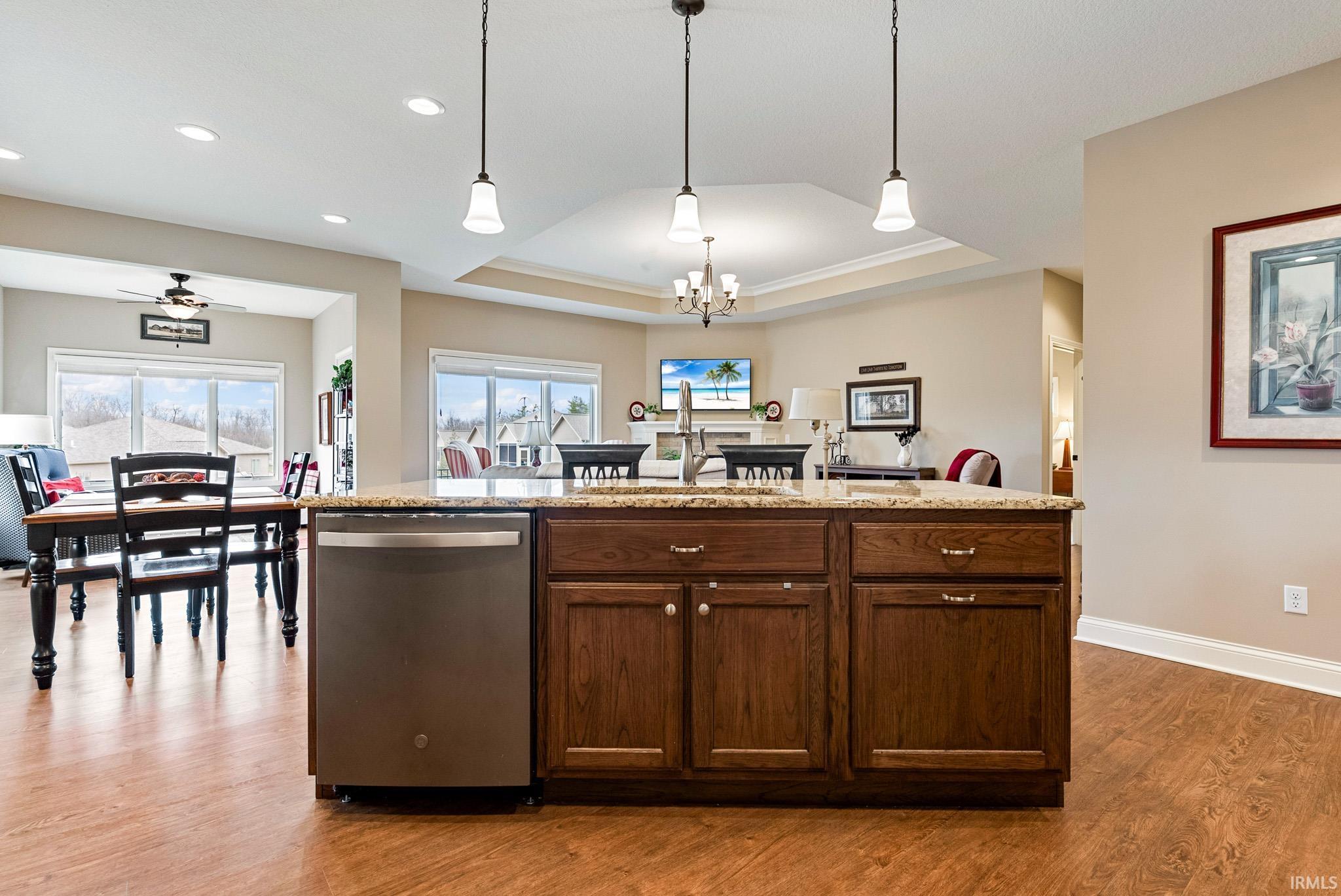 Kitchen featuring dishwasher, a center island with sink, a raised ceiling, light stone countertops, and dark wood-style floors