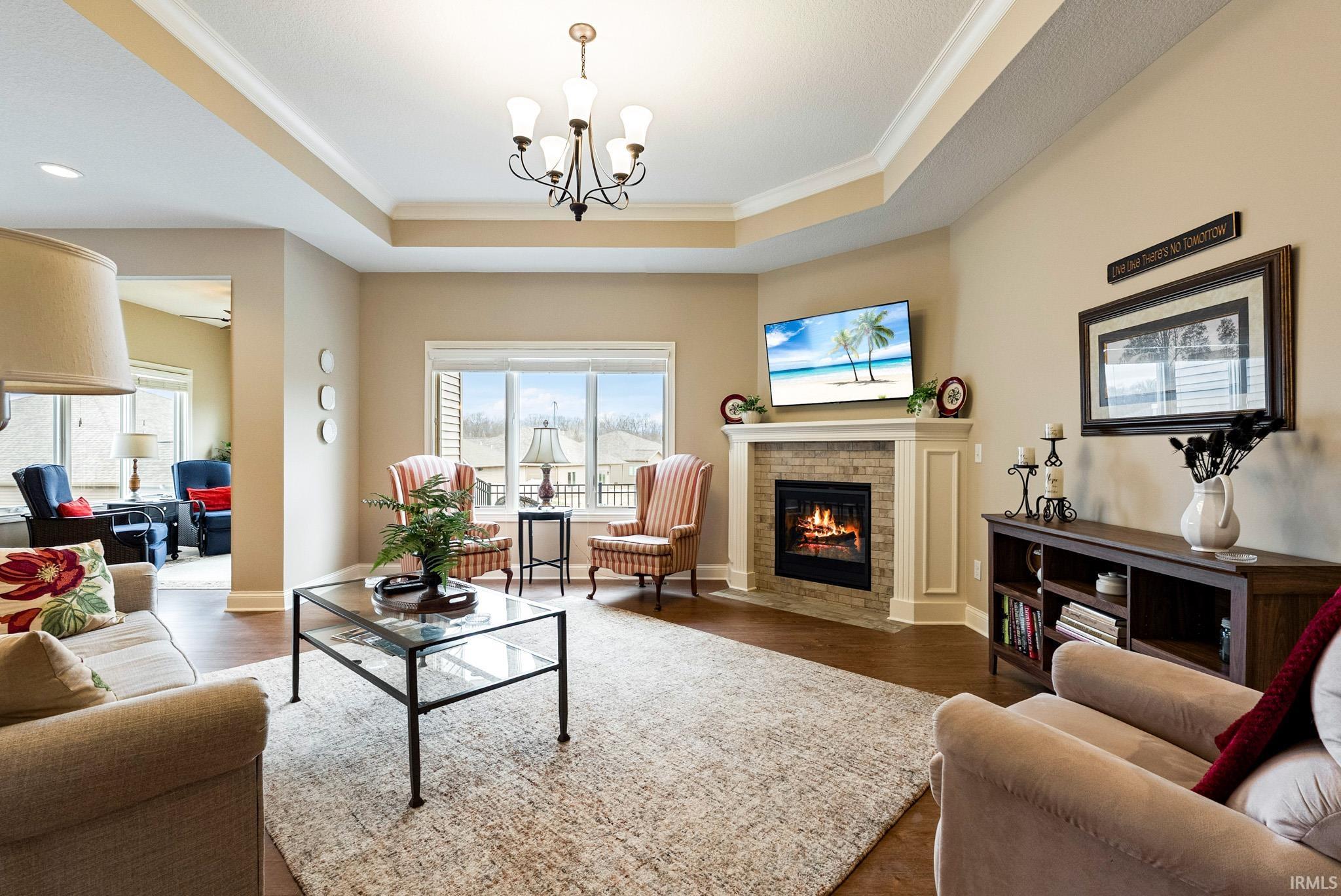 Living area featuring ornamental molding, dark wood-type flooring, a brick fireplace, hanging lights, and a tray ceiling