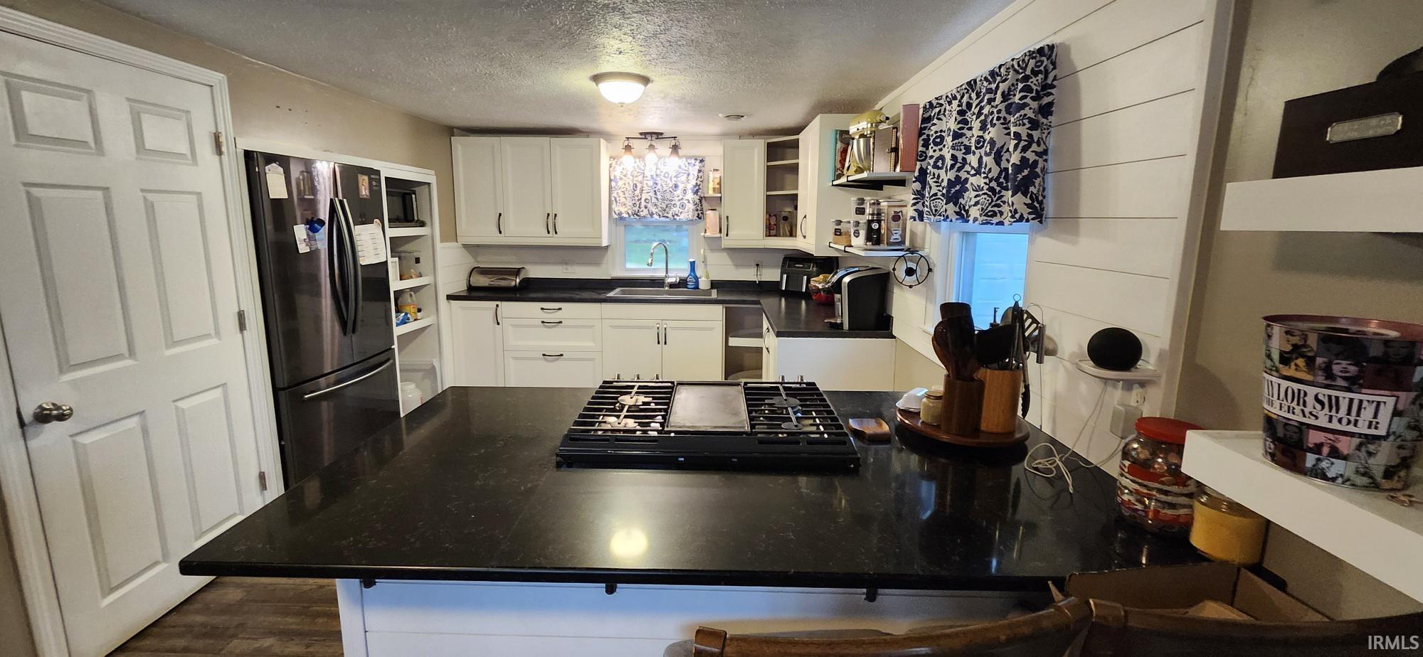 Kitchen featuring white cabinets, black appliances, a textured ceiling, dark countertops, and a kitchen bar