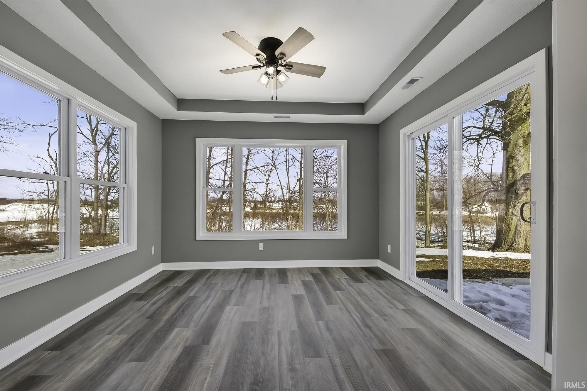 Empty room with a ceiling fan, a raised ceiling, dark wood-style floors, and a water view