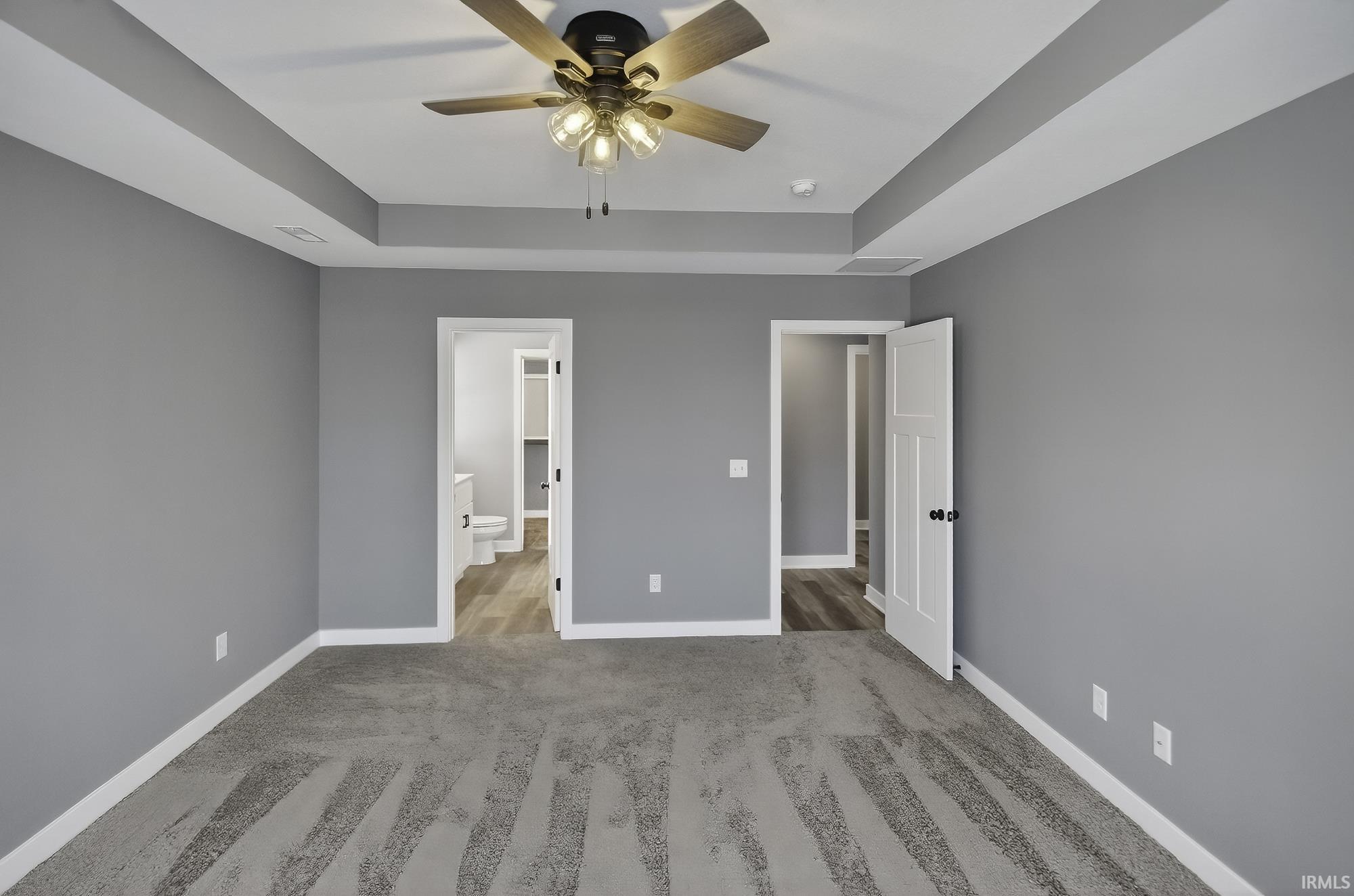 Unfurnished bedroom featuring ensuite bath, light carpet, a ceiling fan, and a tray ceiling