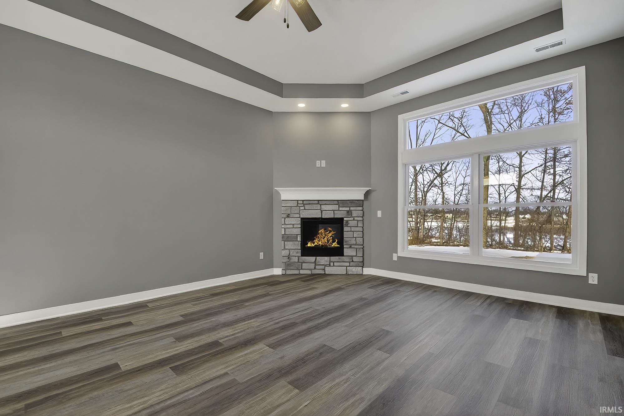 Unfurnished living room with a fireplace, dark wood-style flooring, a tray ceiling, a ceiling fan, and recessed lighting