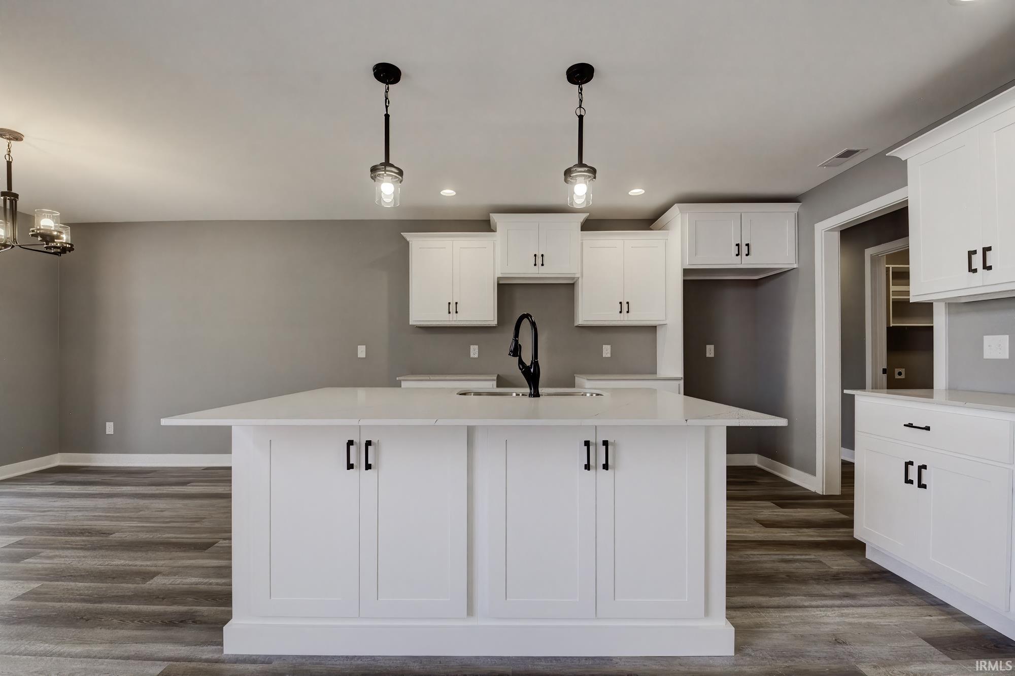 Kitchen with white cabinets, an island with sink, and dark wood-type flooring