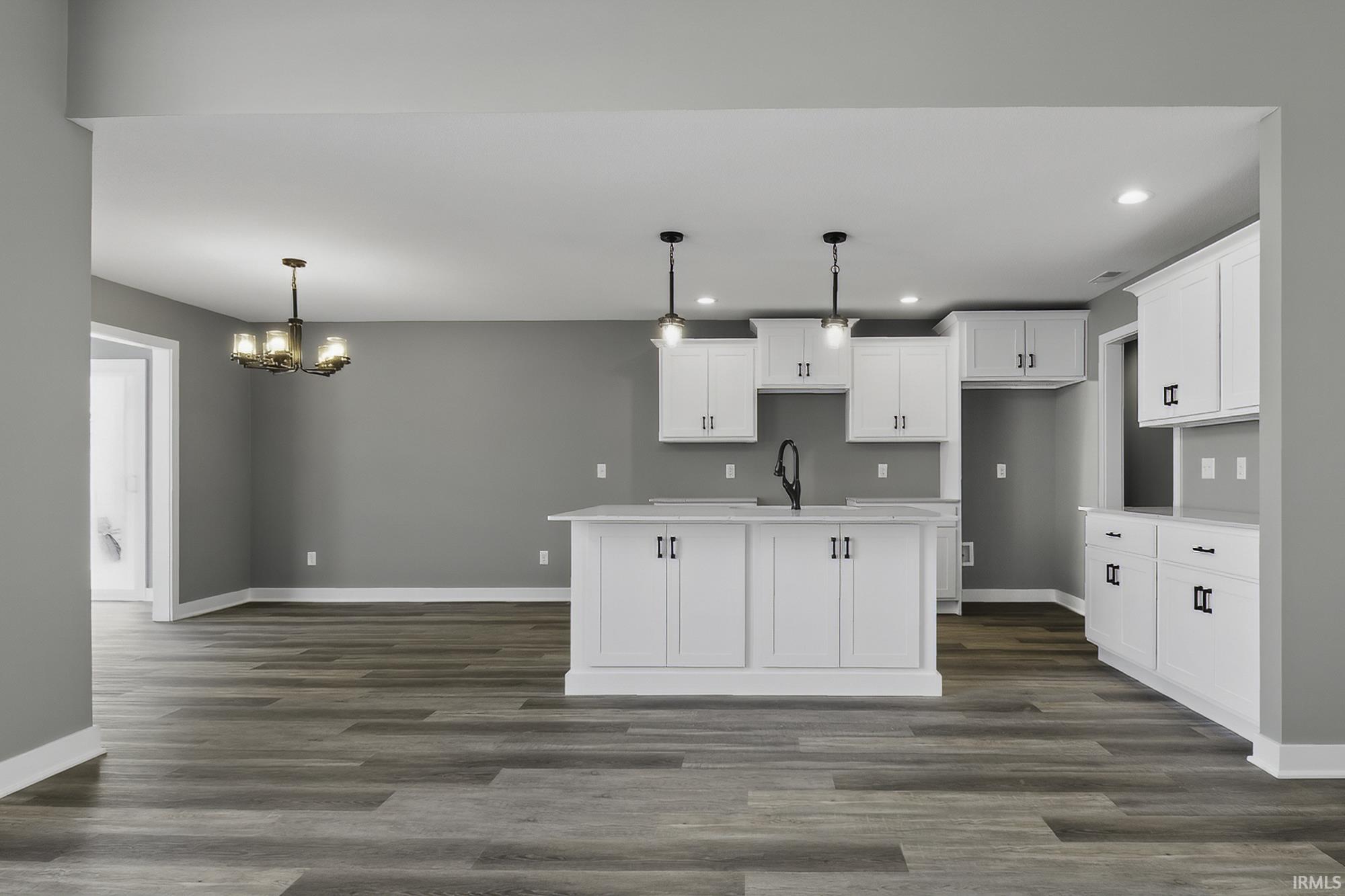 Kitchen featuring white cabinets, dark wood finished floors, a center island with sink, suspended lighting, and light stone counters