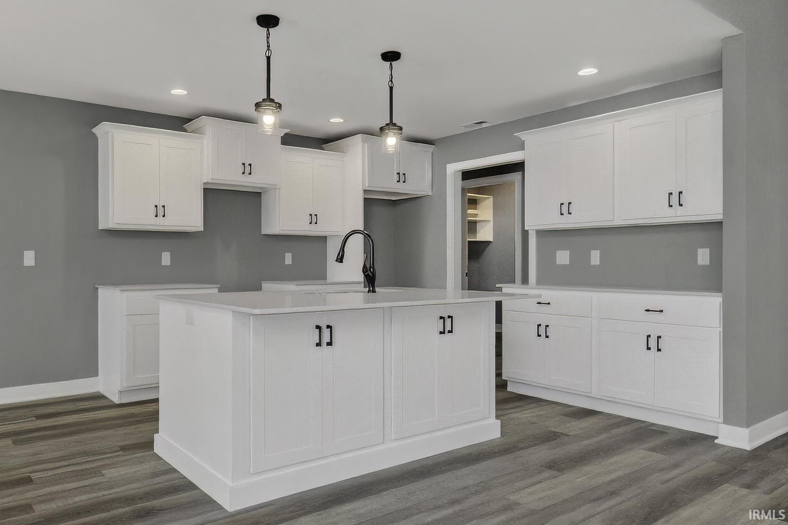 Kitchen with white cabinets, a center island with sink, decorative light fixtures, dark wood finished floors, and light stone counters