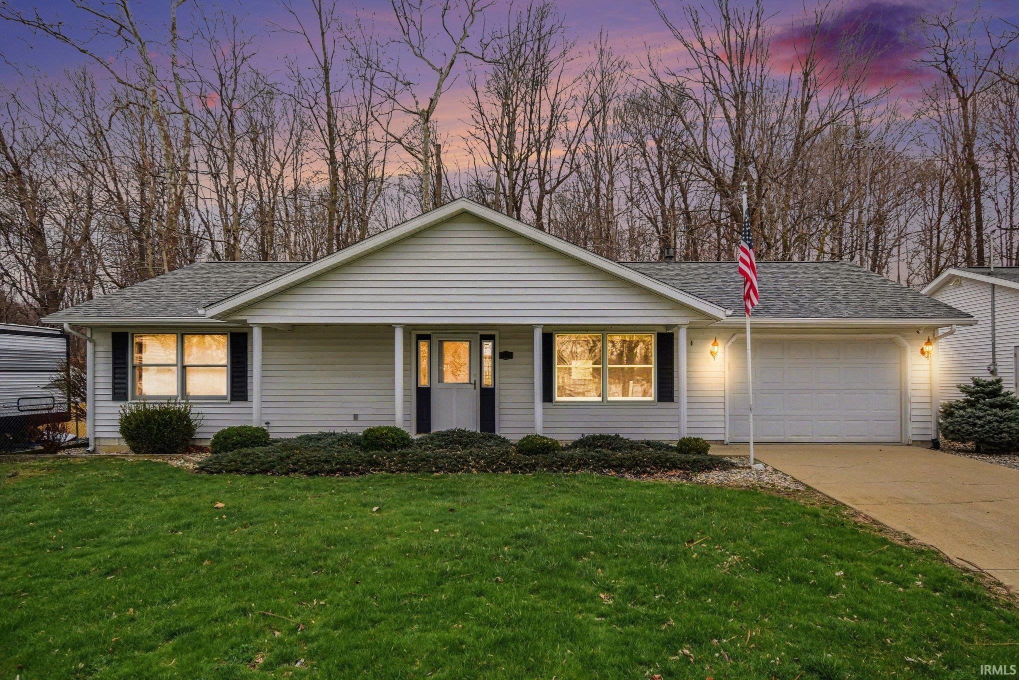 View of front of home featuring roof with shingles, an attached garage, a porch, a front yard, and driveway