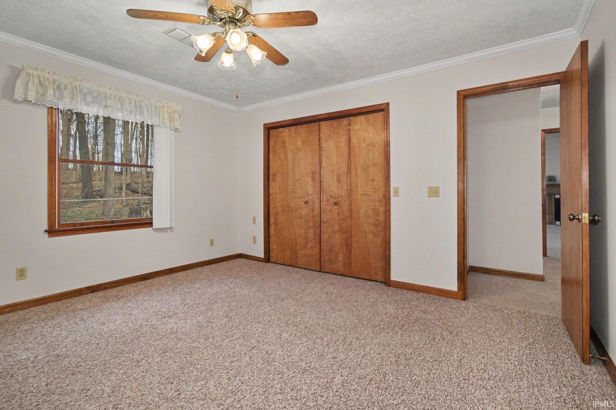 Unfurnished bedroom with a closet, light colored carpet, a textured ceiling, ceiling fan, and crown molding