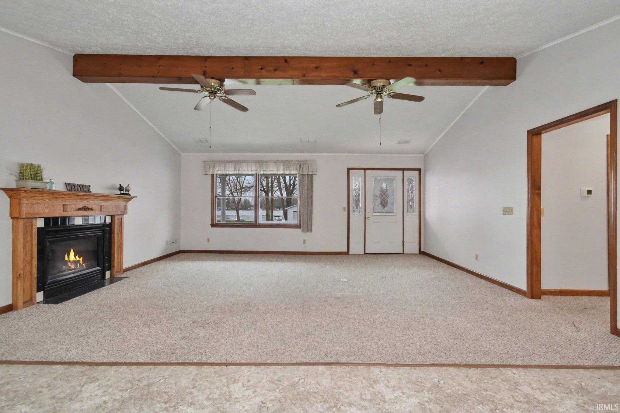 Unfurnished living room with beamed ceiling, a fireplace with flush hearth, and light carpet